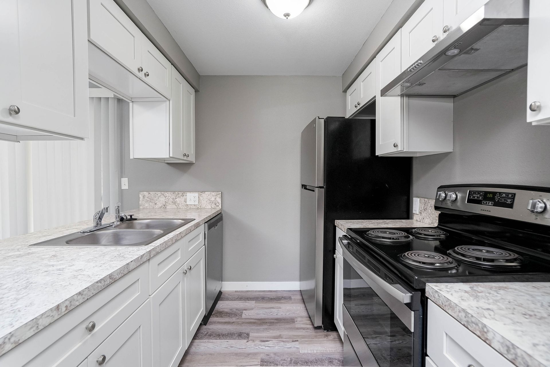 Narrow modern kitchen with white cabinets, black stove and refrigerator, and light countertops