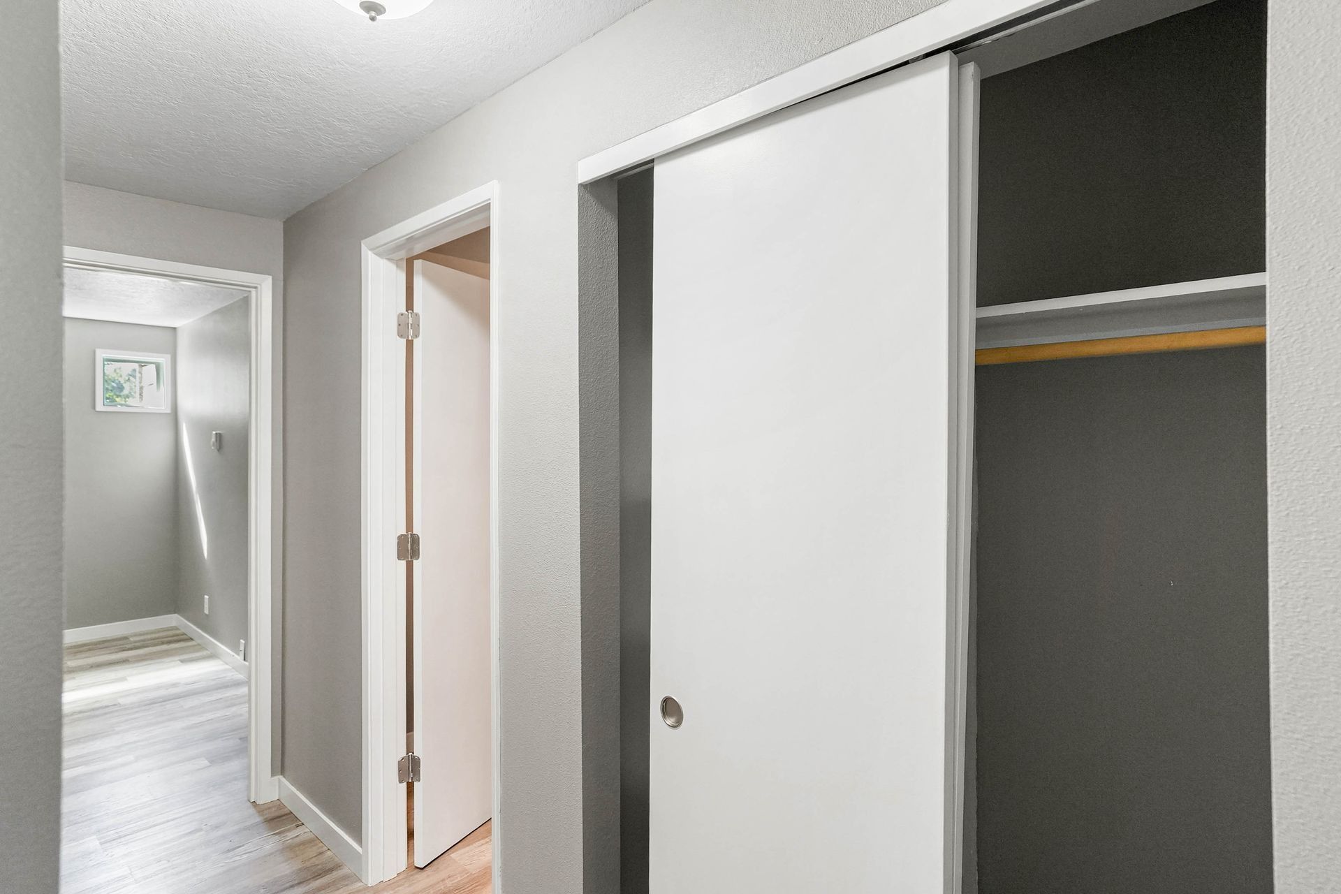 Hallway with gray walls, white doors, and an open closet showing a wooden shelf