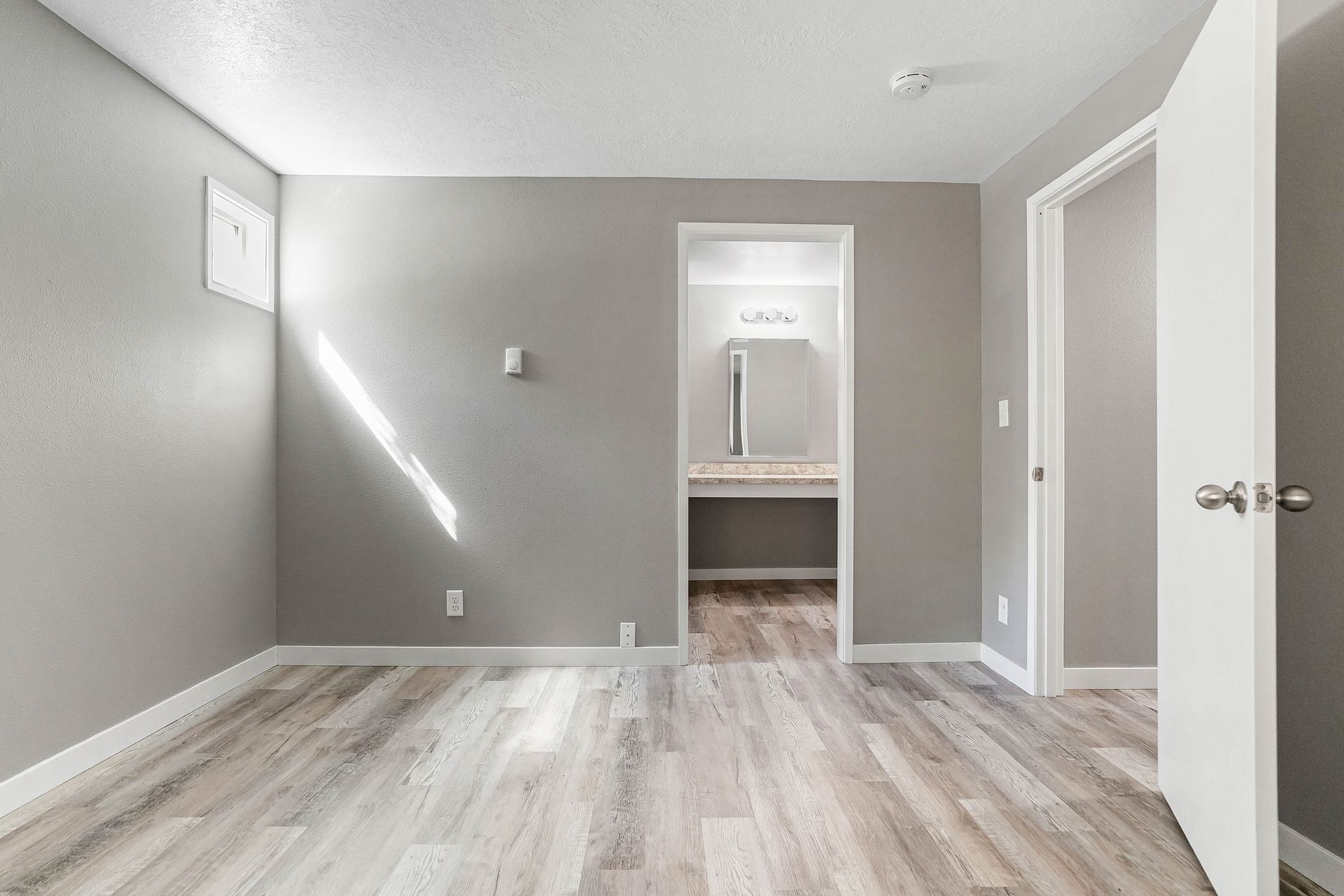 Empty gray bedroom with light wood floors and a doorway to a bathroom or closet.