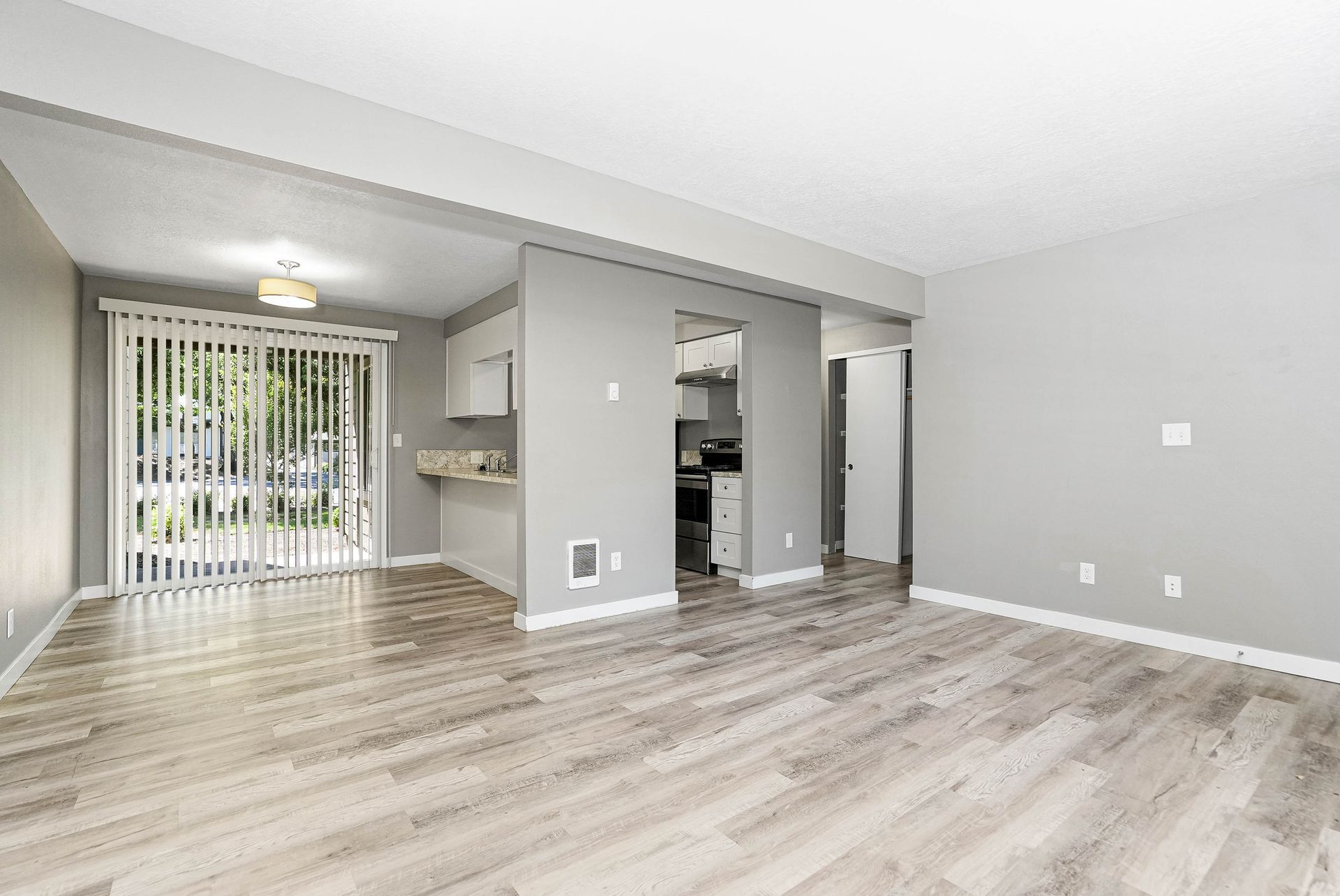 Empty modern living room with light wood floors, gray walls, and sliding glass doors to a patio.