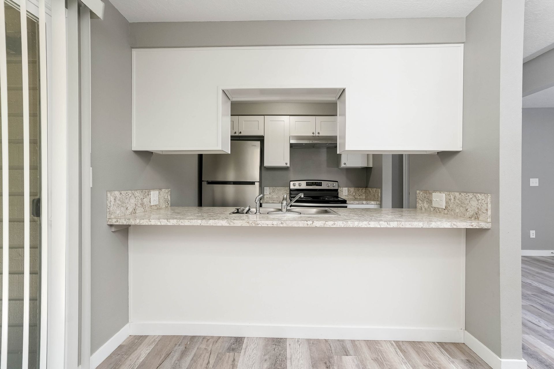 Empty modern kitchen pass-through with white cabinets, granite counter, and light wood flooring
