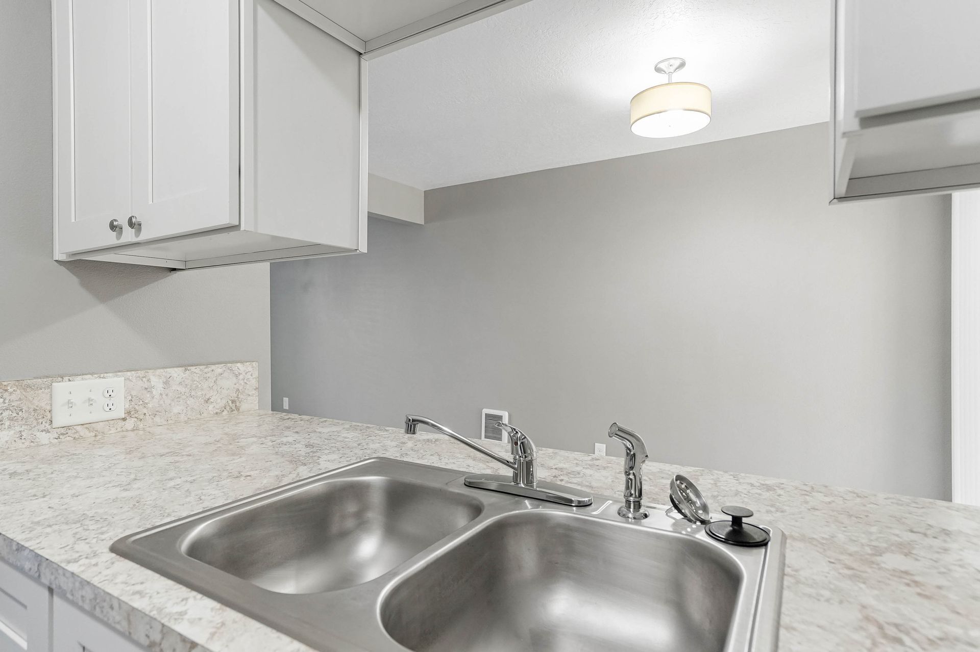 Modern kitchen sink with double basin, white cabinets, and speckled countertop