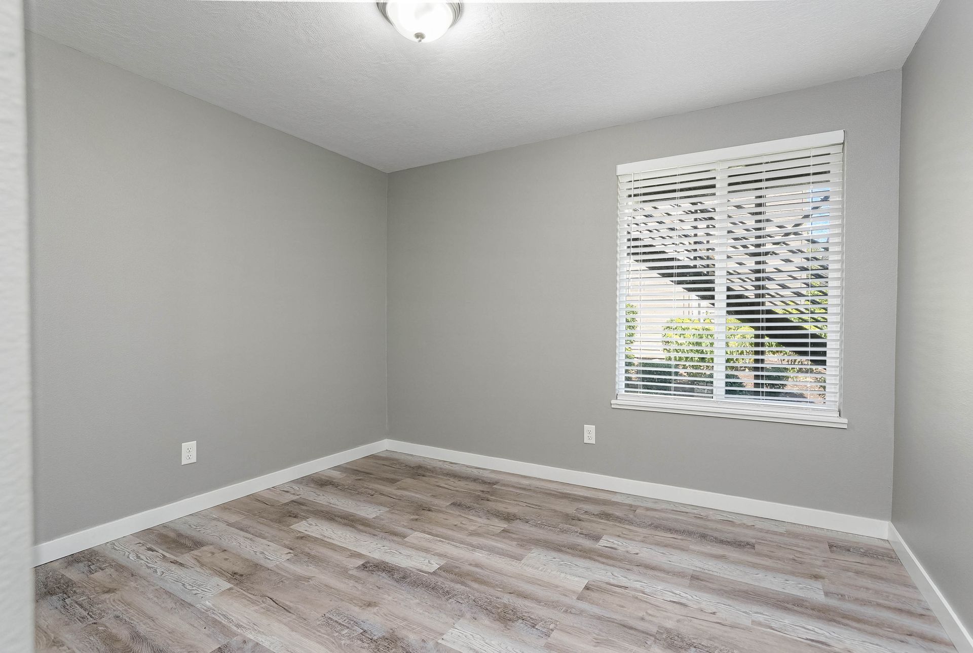 Empty gray bedroom with white blinds and wood-look flooring