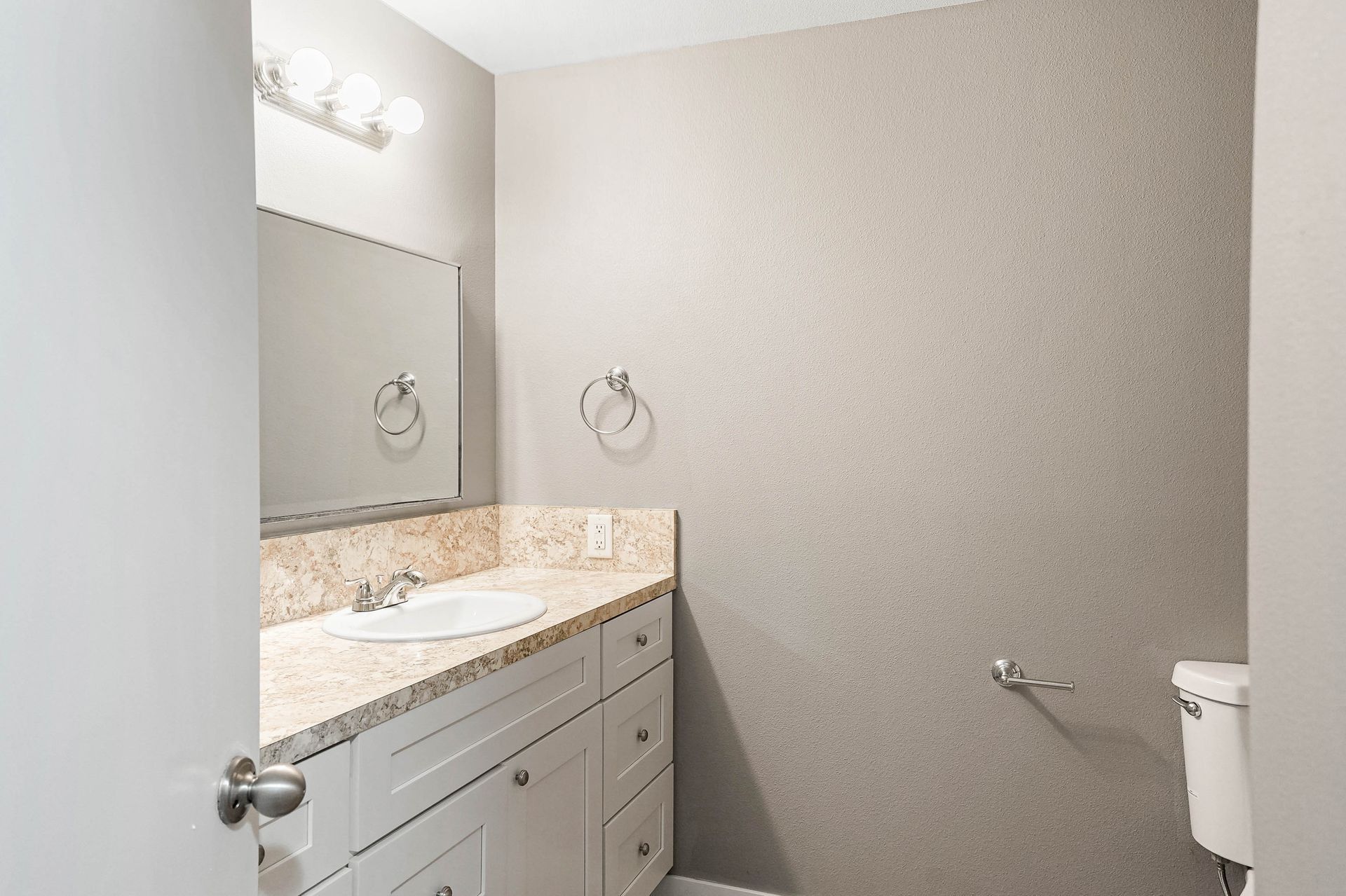 Modern bathroom vanity with beige countertop, mirror, gray walls, and white toilet paper holder.