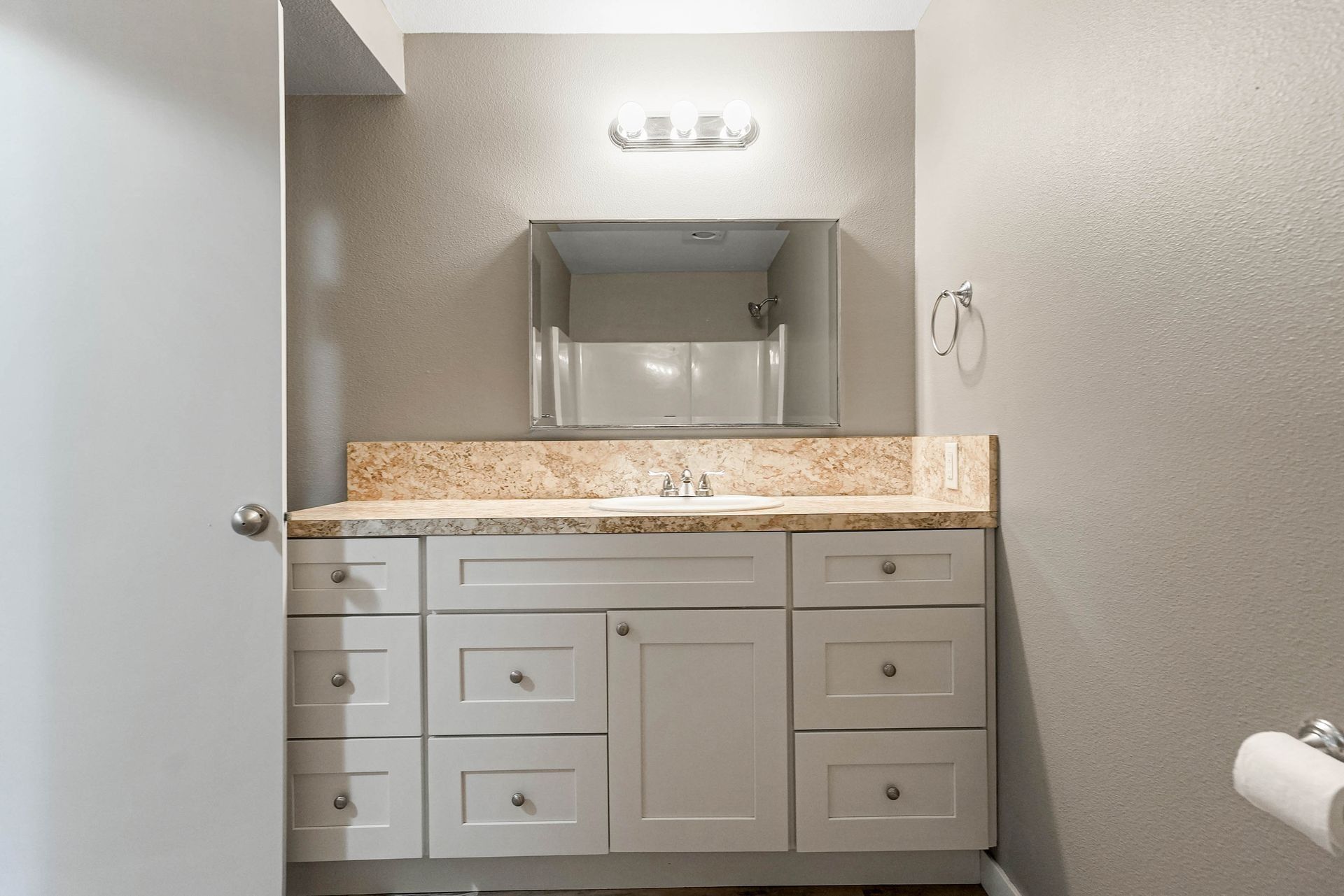 Bathroom vanity with white cabinets, granite countertop, and large mirror above a sink.