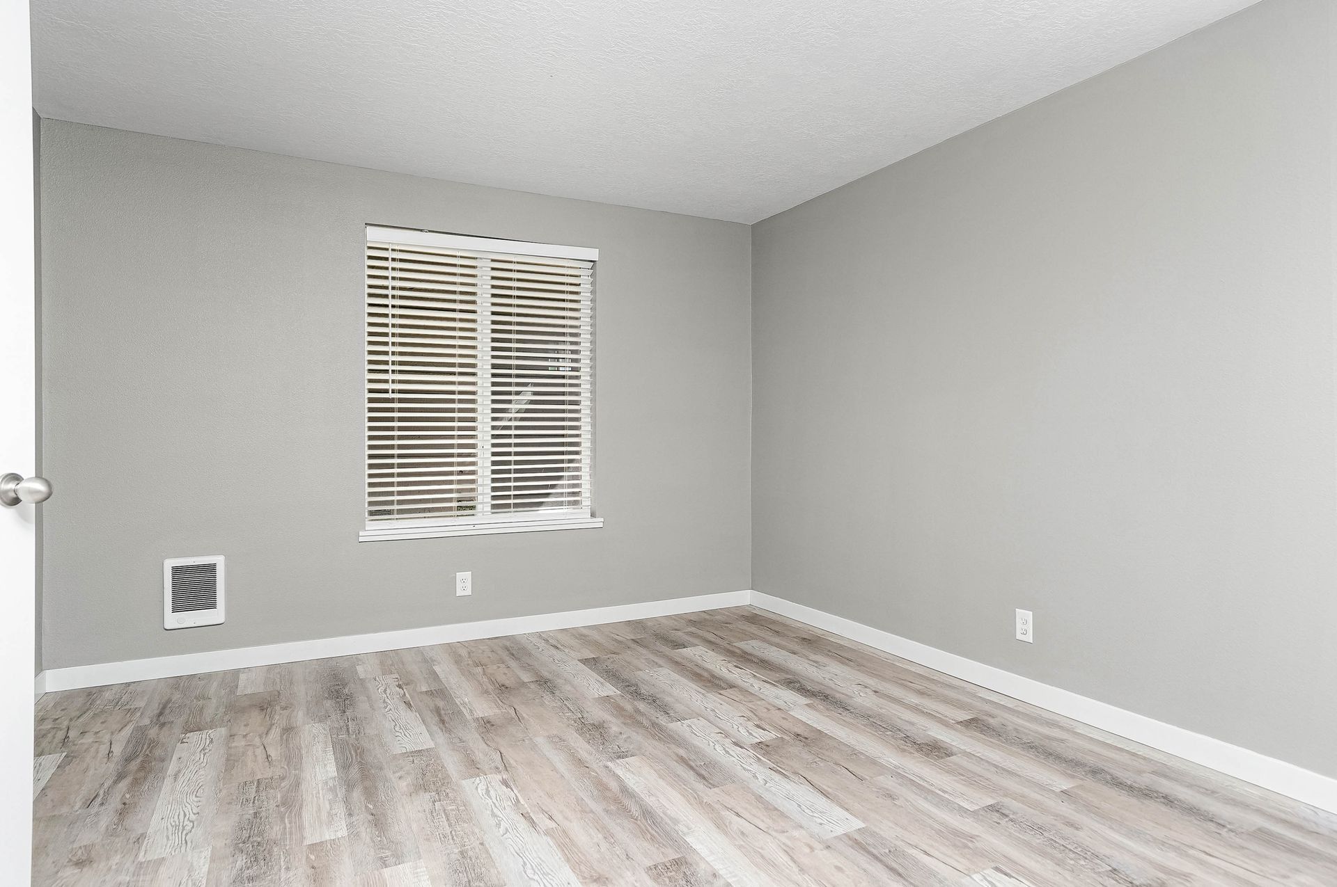 Empty gray room with wood-look flooring and a window with blinds