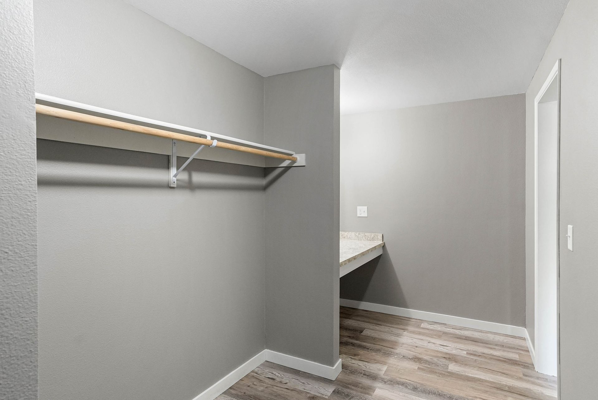 Empty walk-in closet with gray walls, white shelves, and wood-look flooring