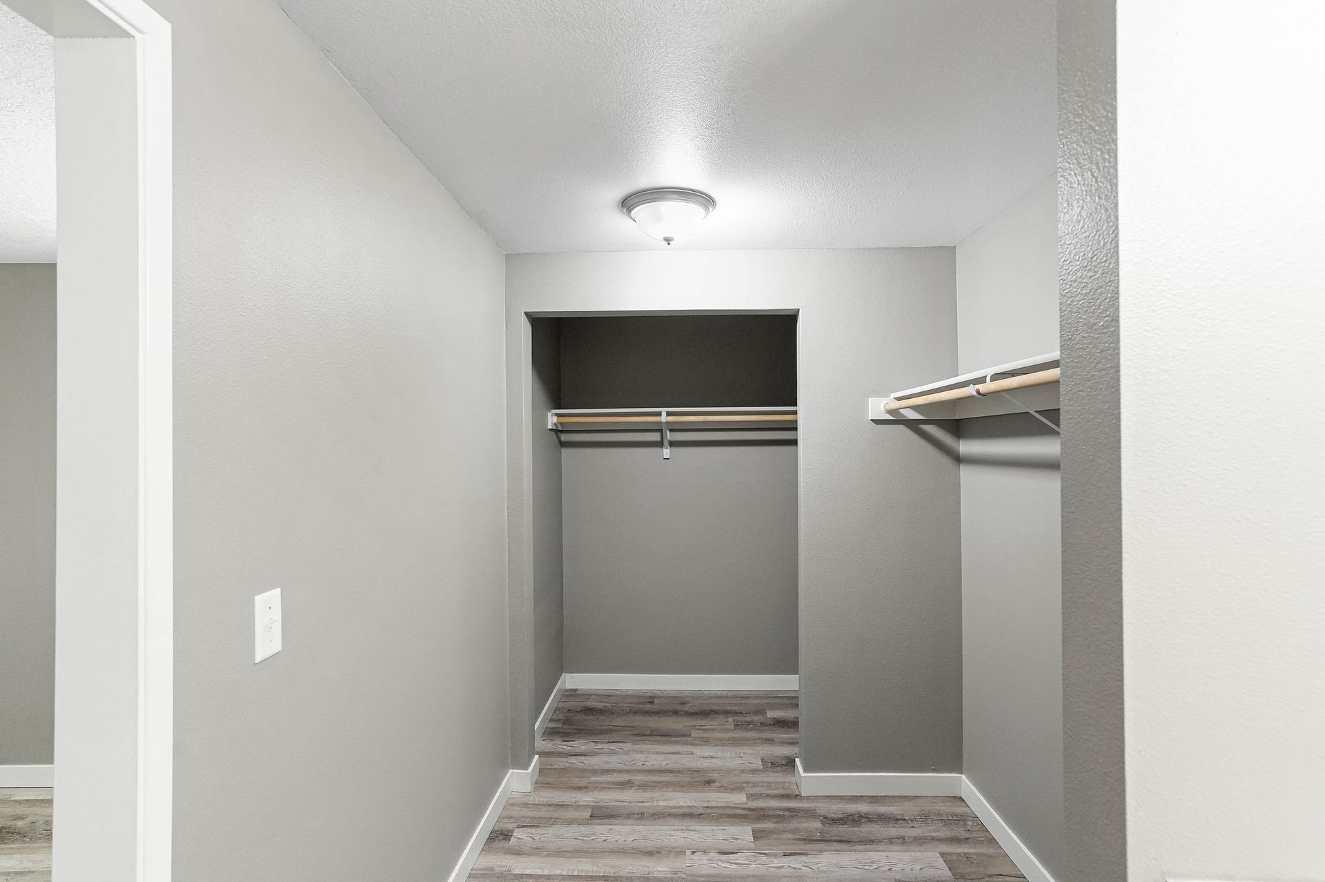 Empty walk-in closet with gray walls, white trim, hanging rods, and wood-look flooring.