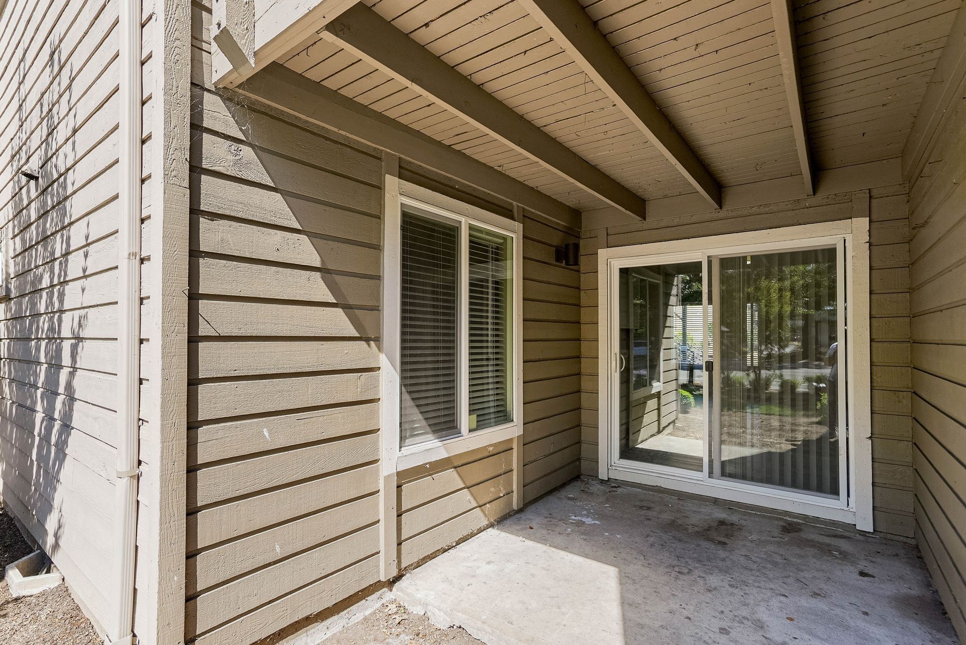 Covered patio with beige siding, white-framed windows, and sliding glass doors leading outside