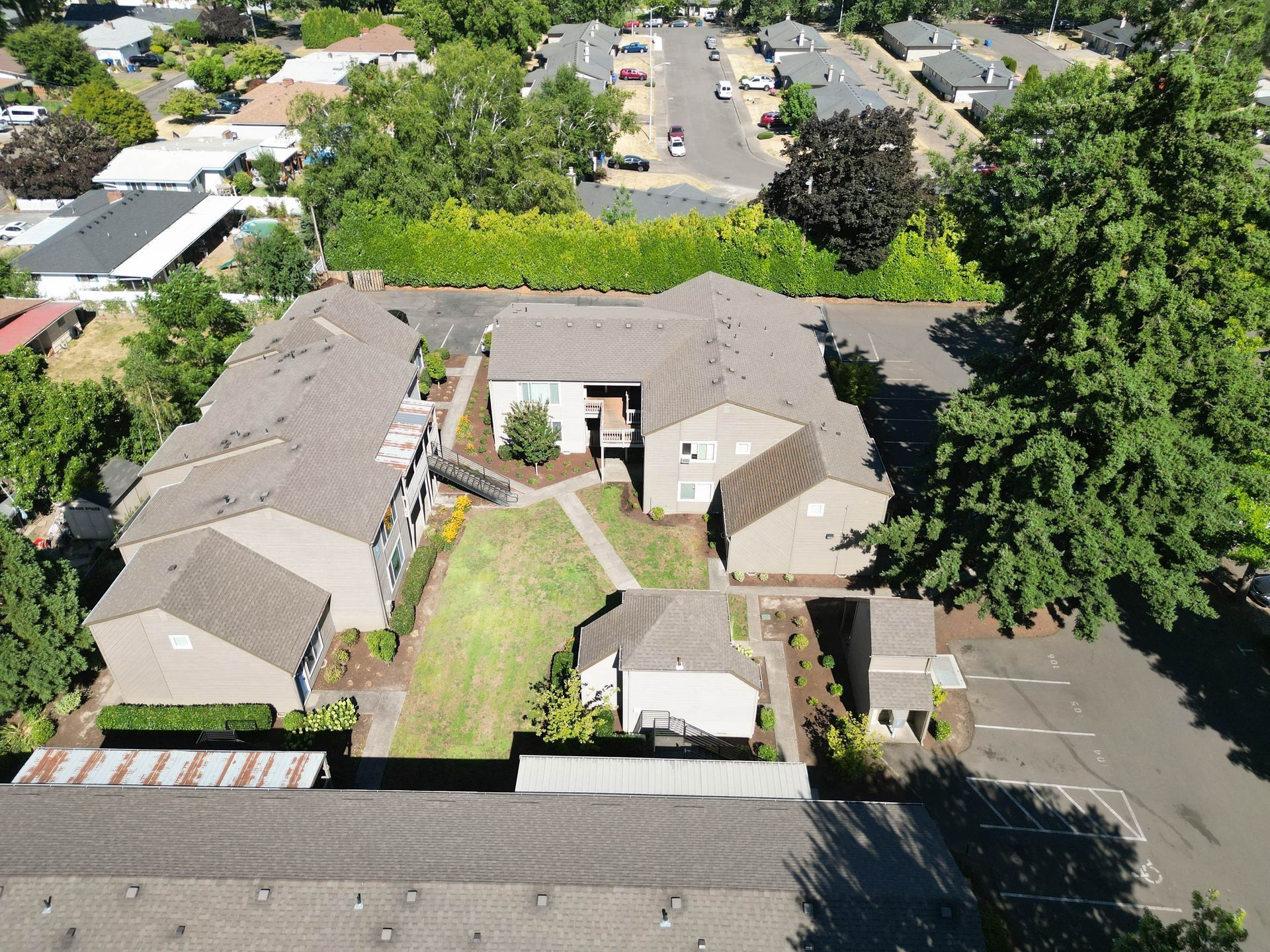 Aerial view of a suburban townhouse complex with parked cars, trees, and surrounding homes.