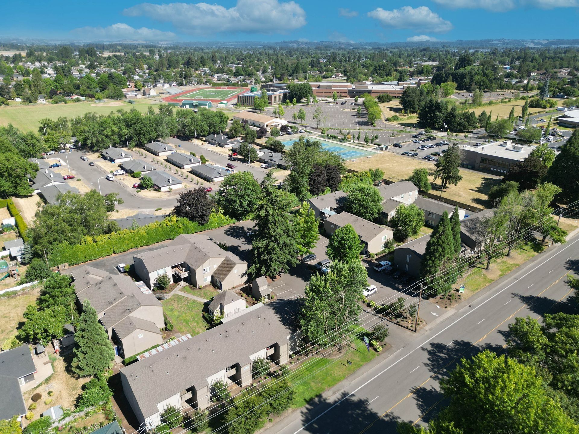 Aerial view of a suburban neighborhood with apartments, trees, roads, and distant hills under a blue sky