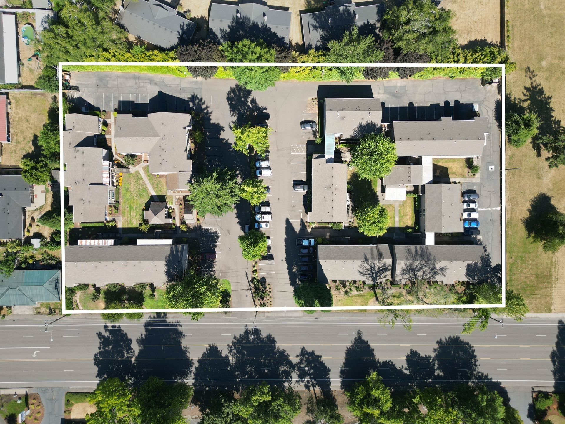 Aerial view of two apartment buildings in a tree-lined residential lot beside a road