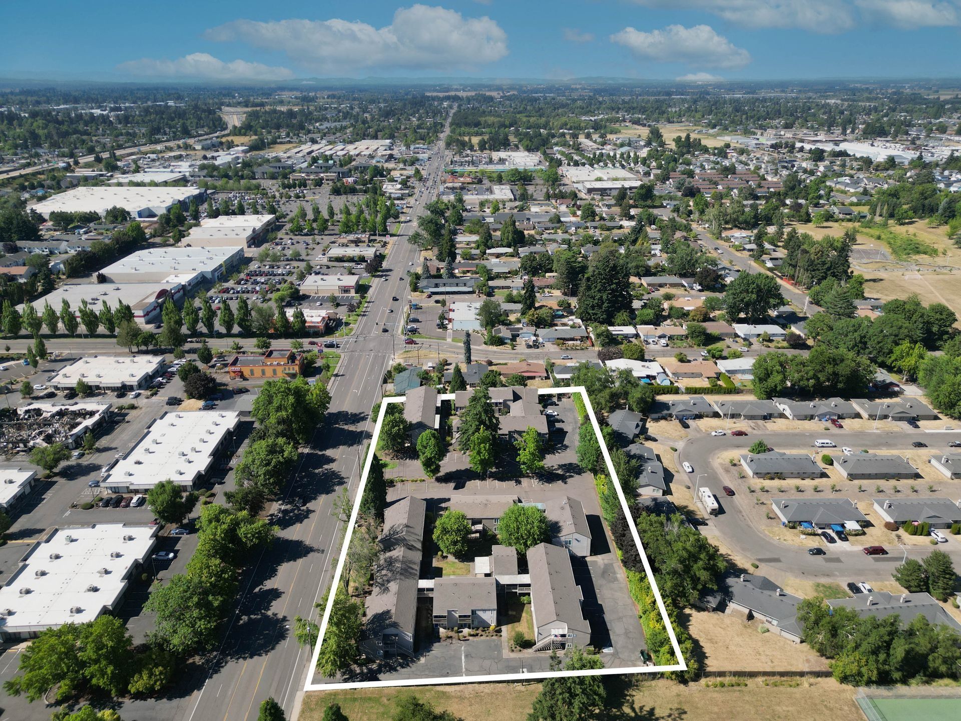 Aerial view of a suburban neighborhood with tree-lined streets and a wide central road, framed by mountains in the distance