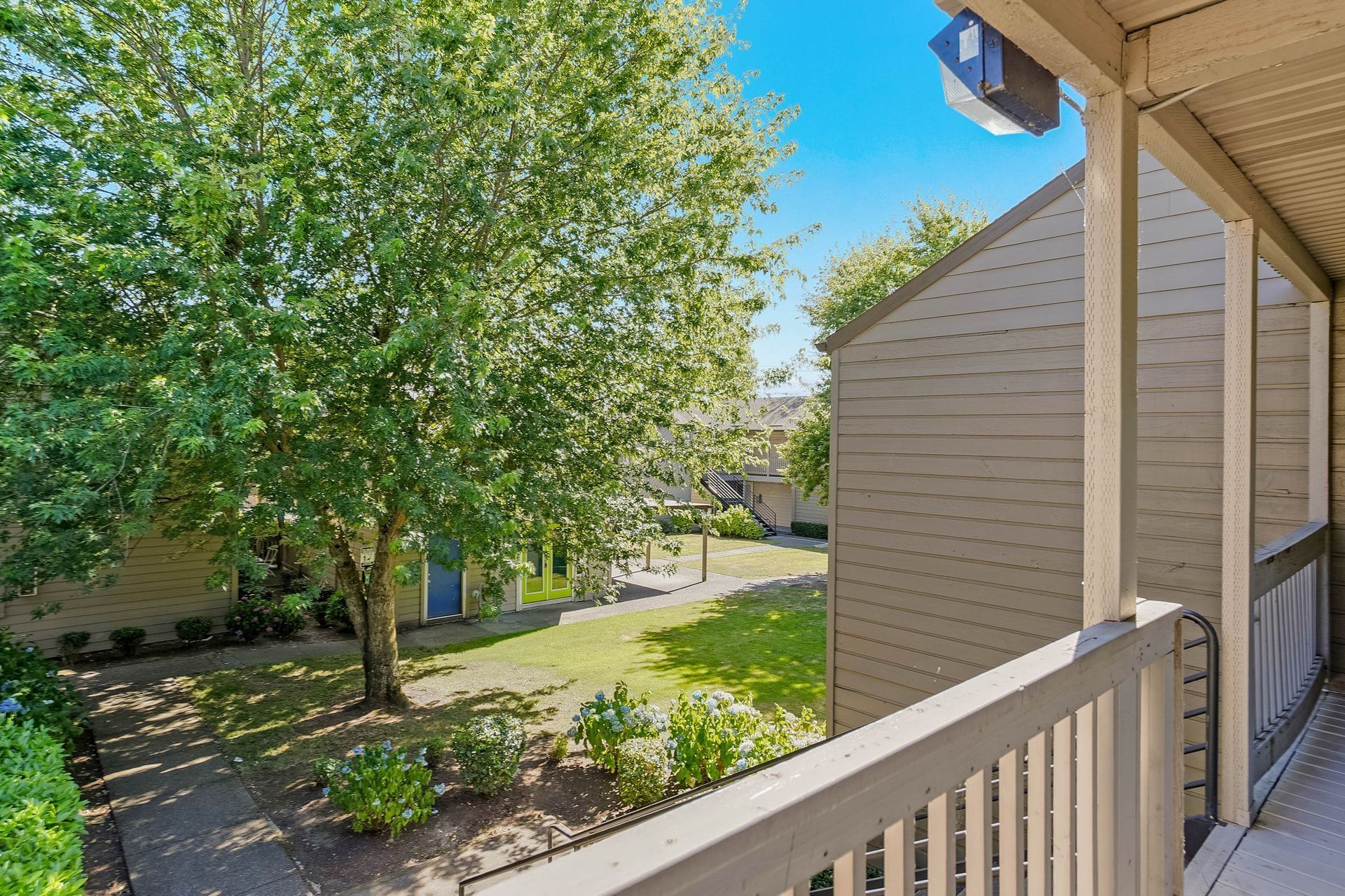 Apartment balcony overlooking a leafy courtyard with trees, grass, and neighboring buildings