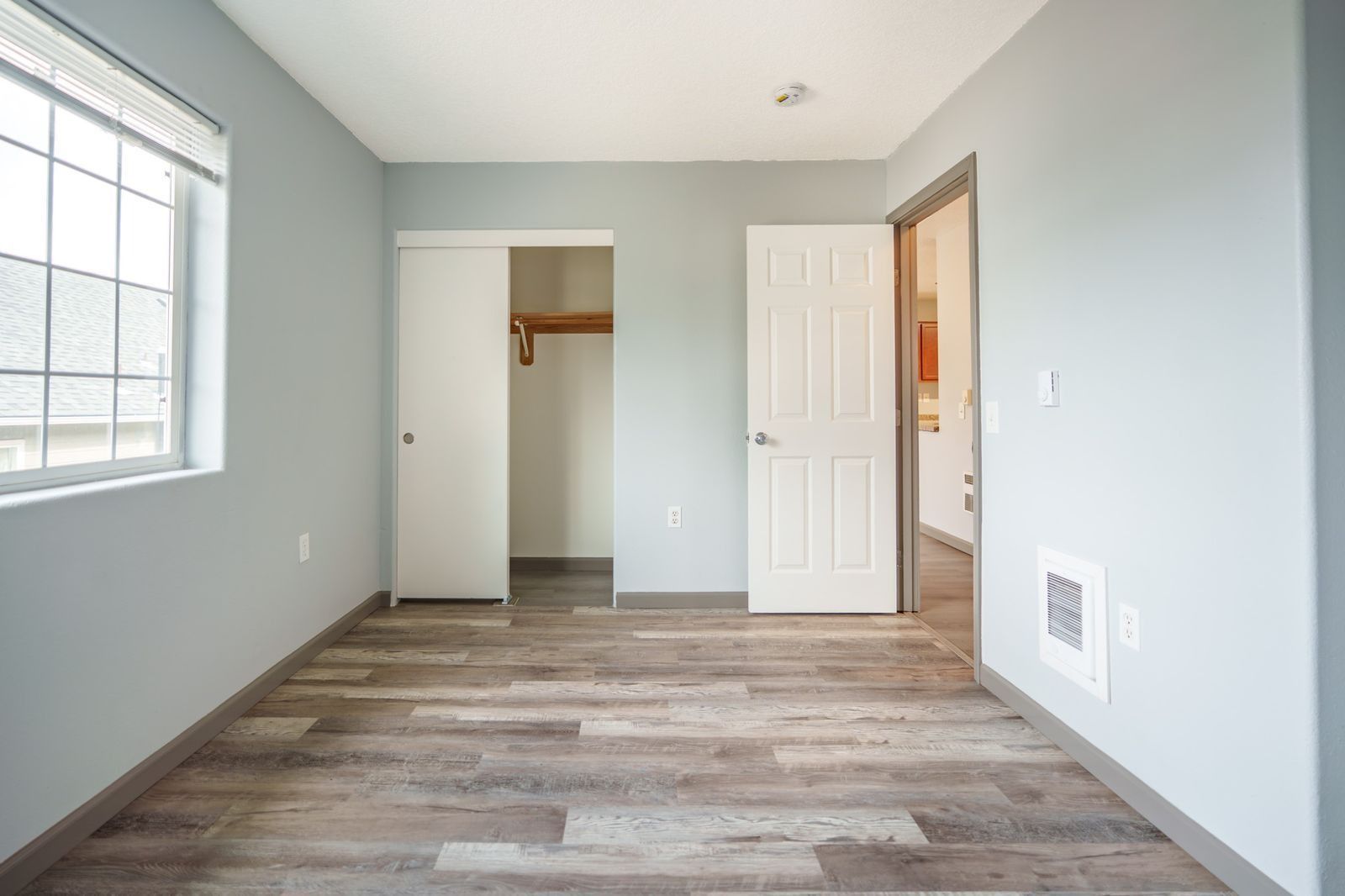 Empty bedroom with gray walls, wood-look flooring, closet, and large window.