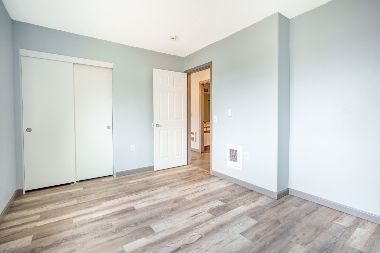 Empty bedroom with light gray walls, wood-look flooring, and a white closet and open doorway