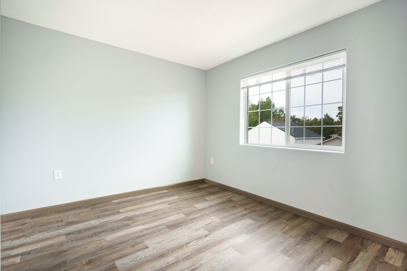 Empty light-gray room with wood-look flooring and a window letting in natural light