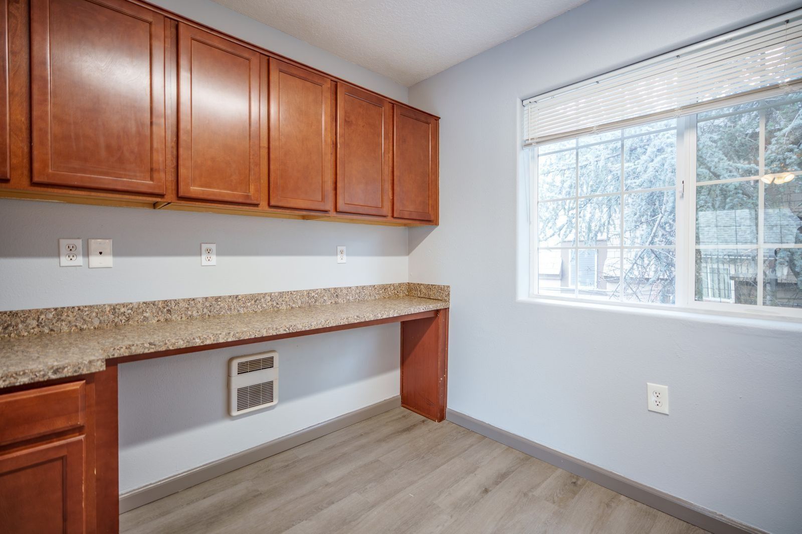 Empty kitchen nook with wood cabinets, speckled countertop, and window by a light gray wall