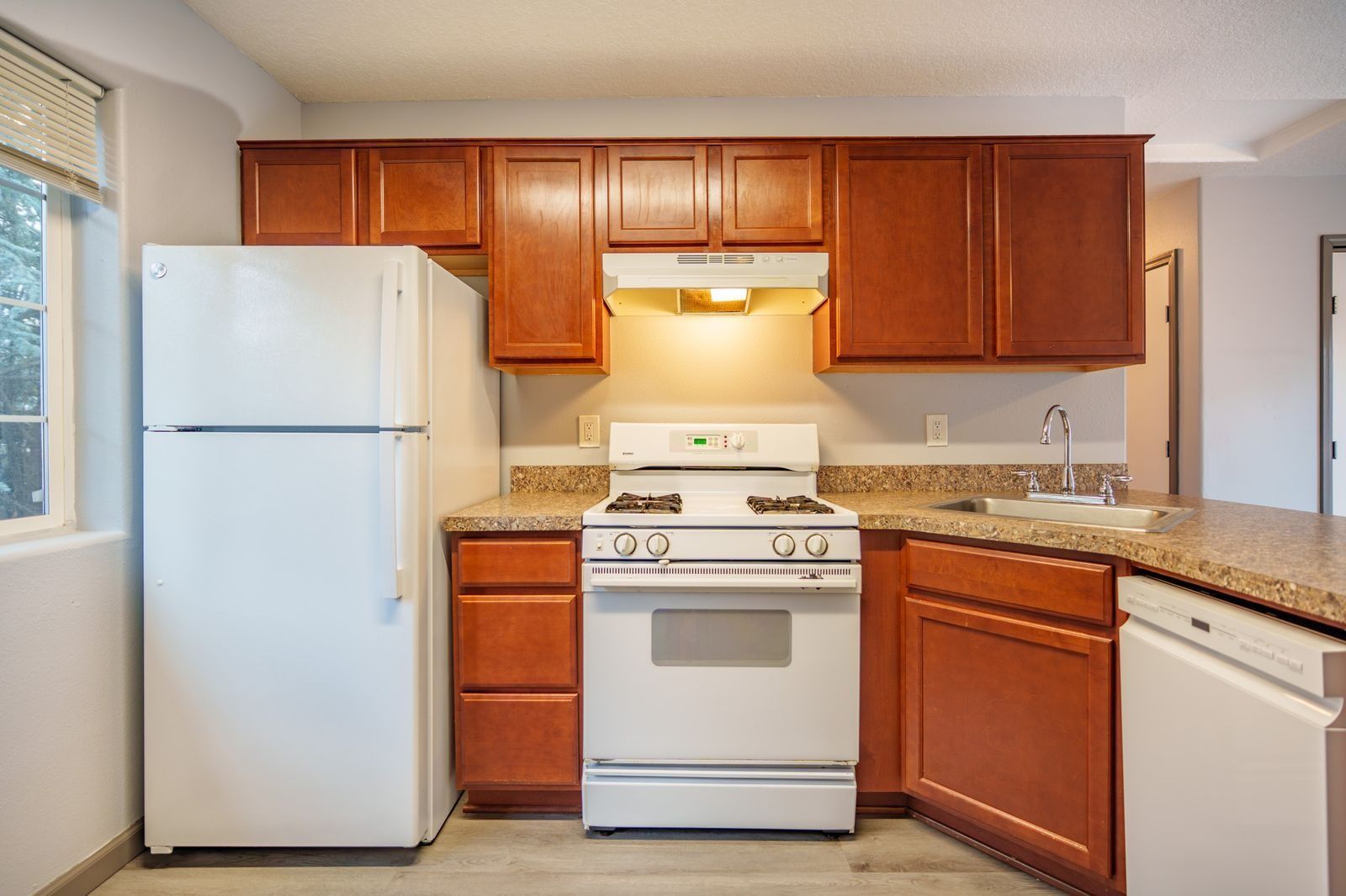 Bright kitchen with white appliances, wood cabinets, and tan countertops.