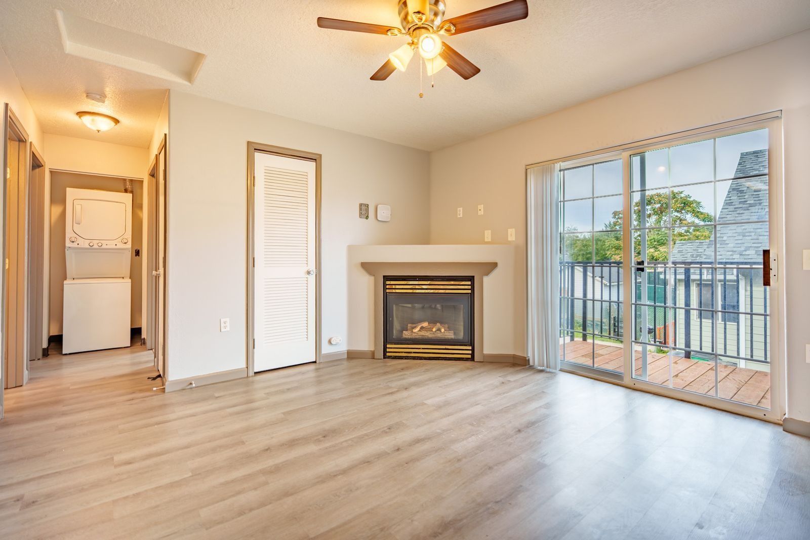 Empty living room with fireplace, ceiling fan, wood floors, and sliding glass doors to a balcony.
