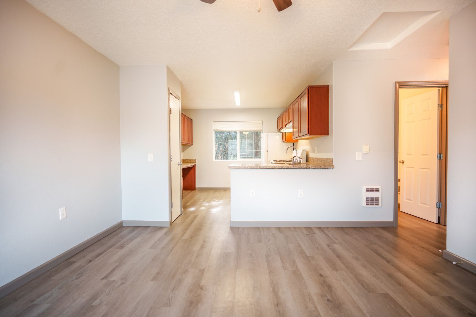 Empty open-plan kitchen and living area with wood floors, white walls, and wood cabinets.