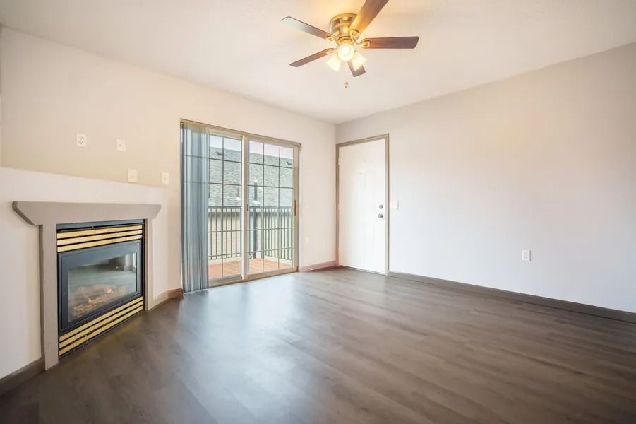 Empty living room with fireplace, ceiling fan, sliding glass door, and wood-look floors