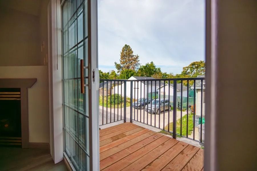 View from an open doorway to a wooden balcony with black railings and parked cars outside.