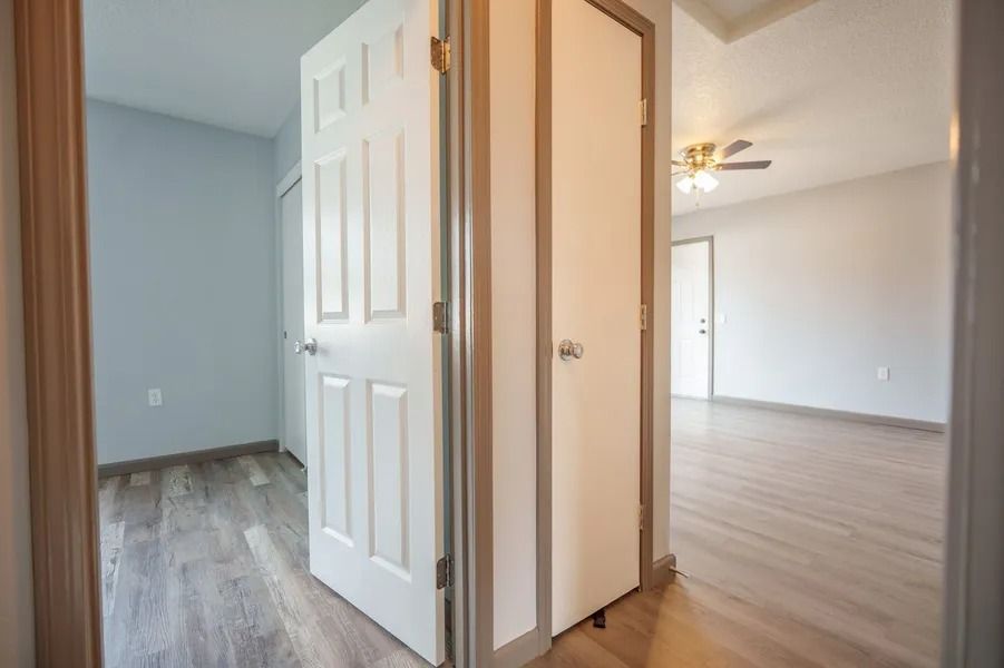 Empty hallway and open doors to two bright rooms with light wood floors and white walls