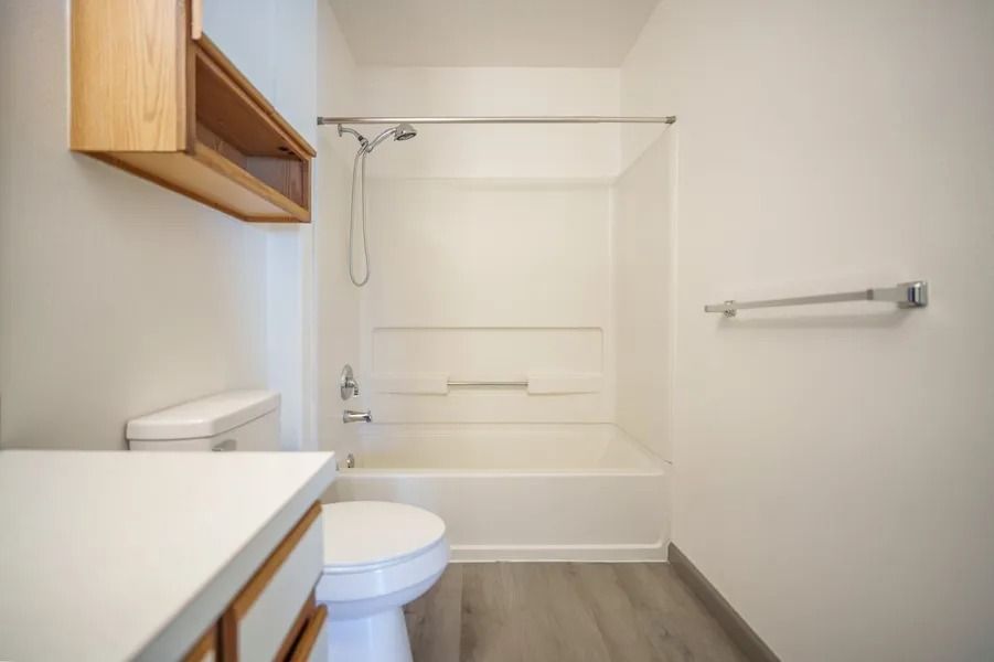 Small bathroom with a white tub-shower, toilet, sink cabinet, and wood accents