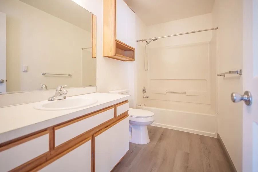 Bright bathroom with white vanity, mirror, toilet, tub, and wood-look flooring