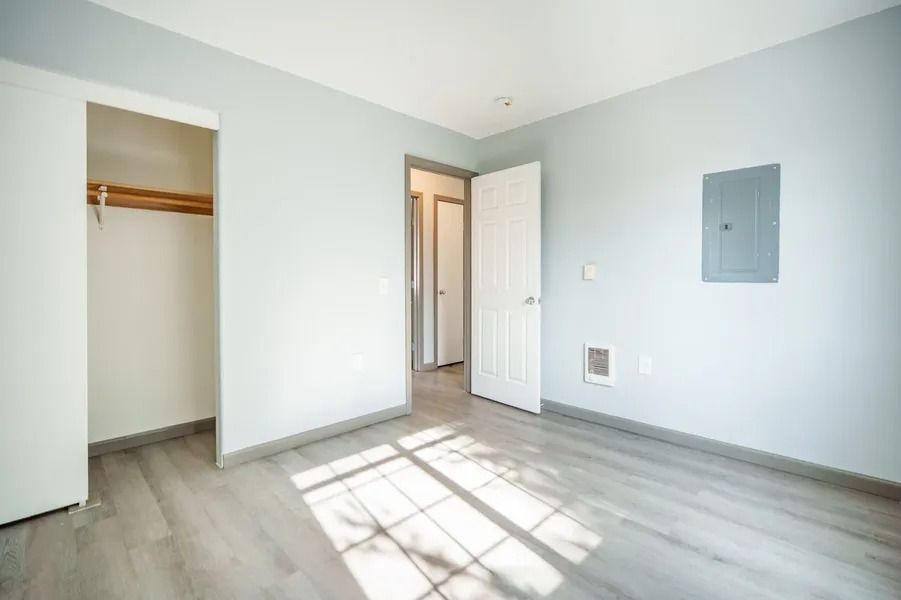 Empty bright room with light wood floors, open closet, and sunlight on the wall.