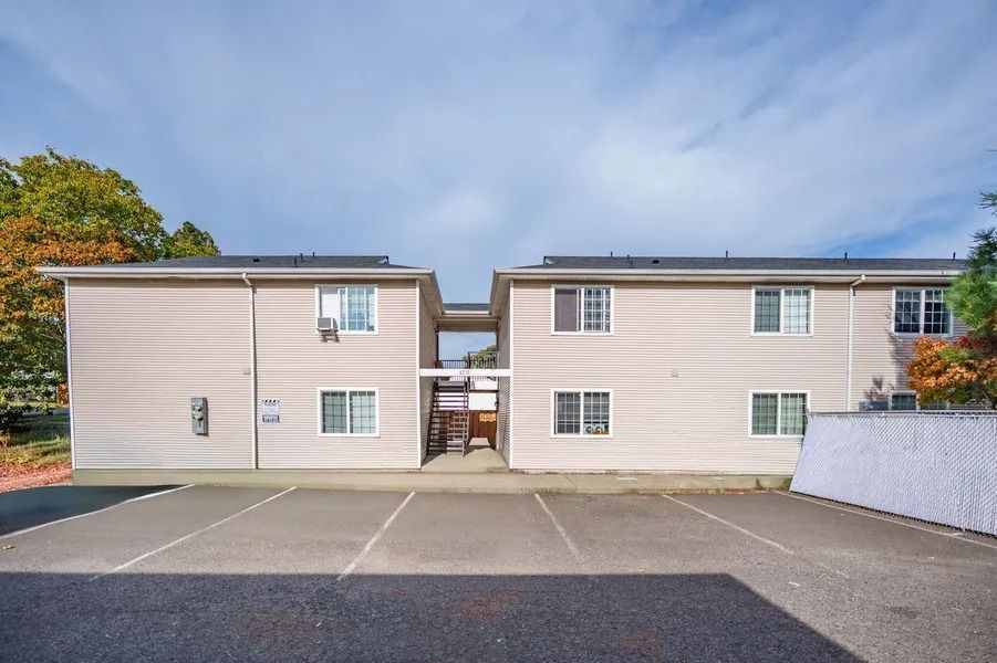 Apartment building with beige siding and a paved parking lot in front under a cloudy sky