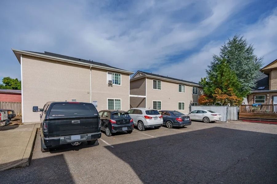 Apartment parking lot with several parked cars and beige townhouses under a blue sky