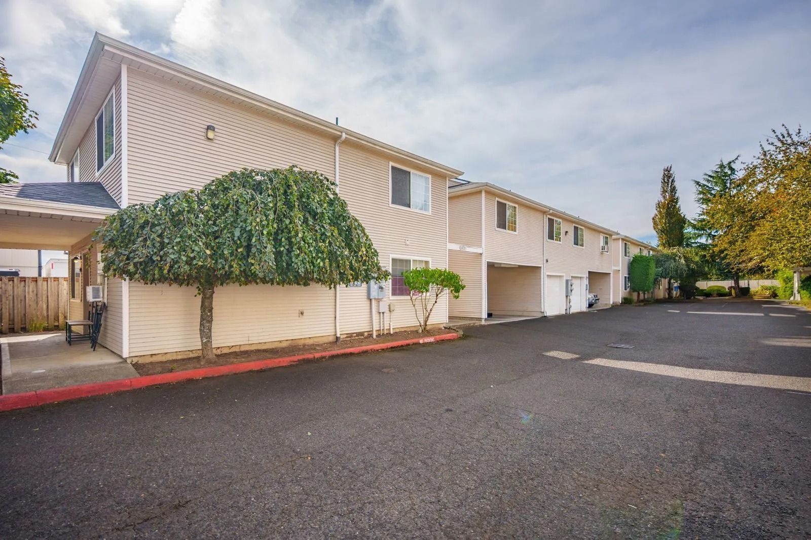 Two-story beige apartment building with green vine-covered trellis and empty parking lot