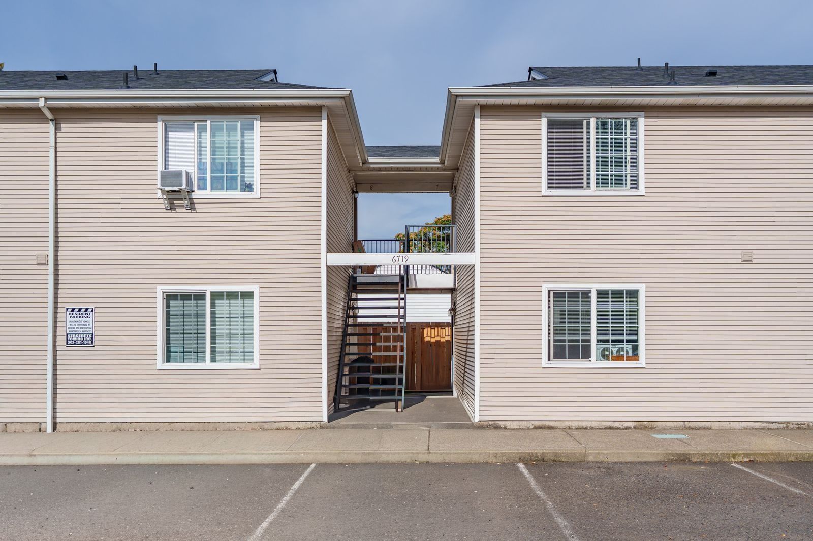 Two beige apartment buildings with a narrow walkway between them and parked cars in front