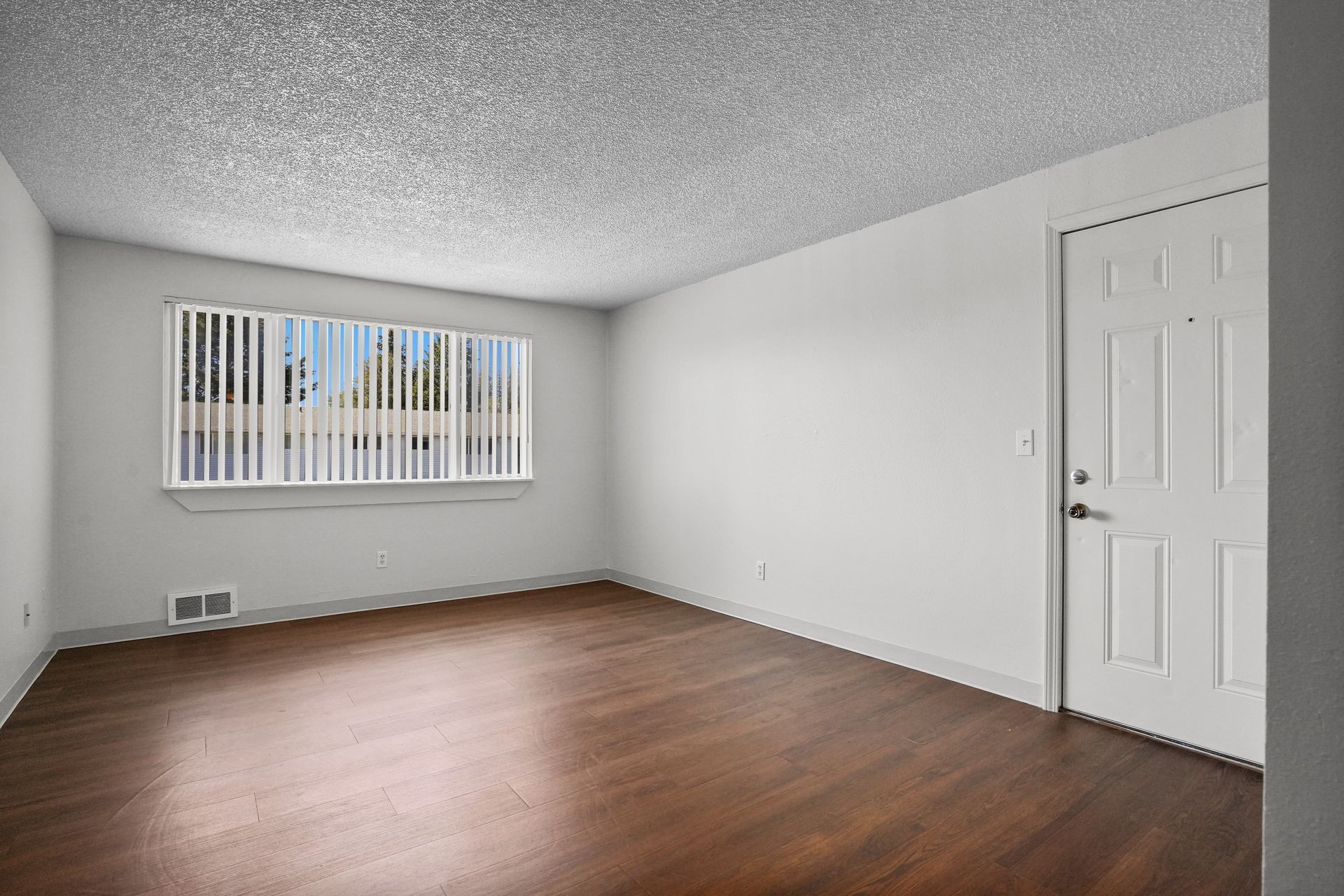 Empty room with wood floor, white walls, window blinds, and a closed door