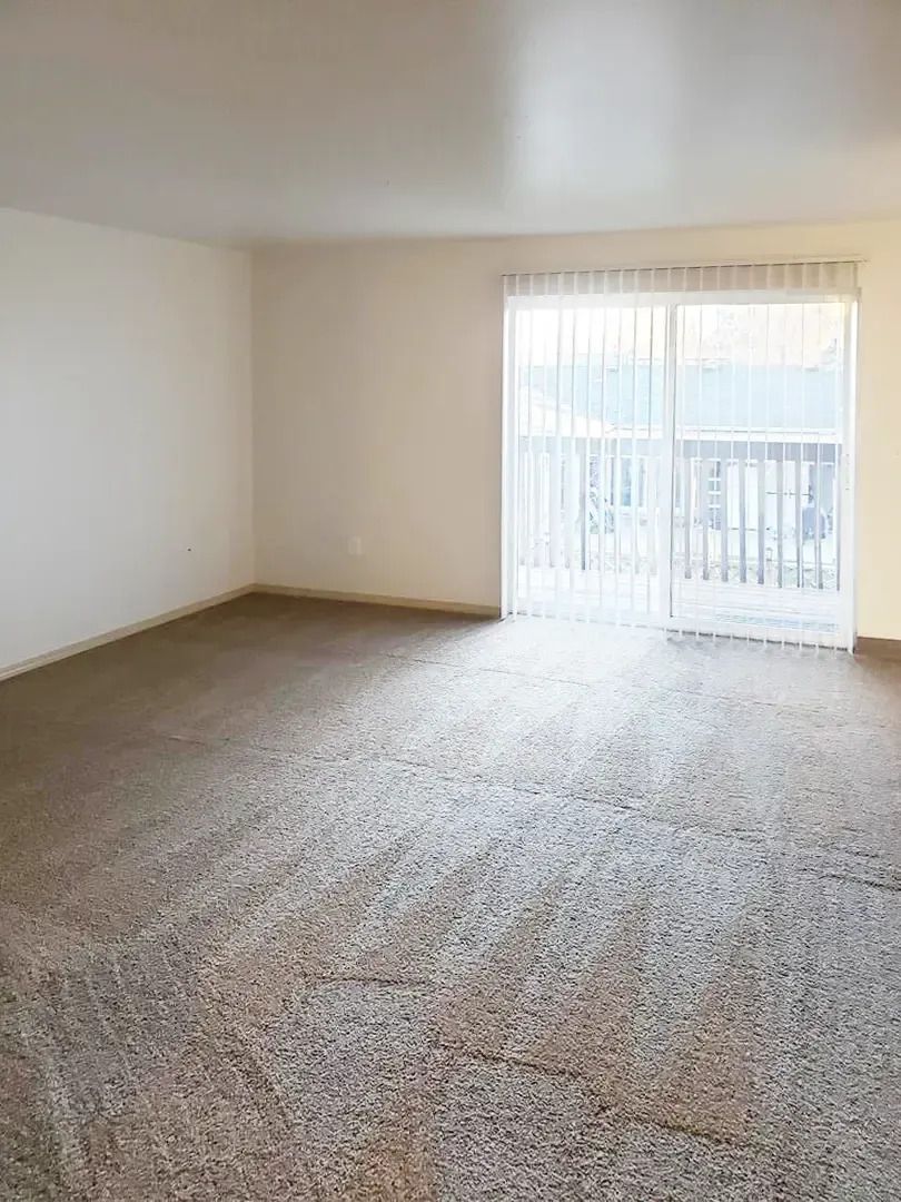 Empty unfurnished living room with beige carpet and sliding glass doors letting in daylight
