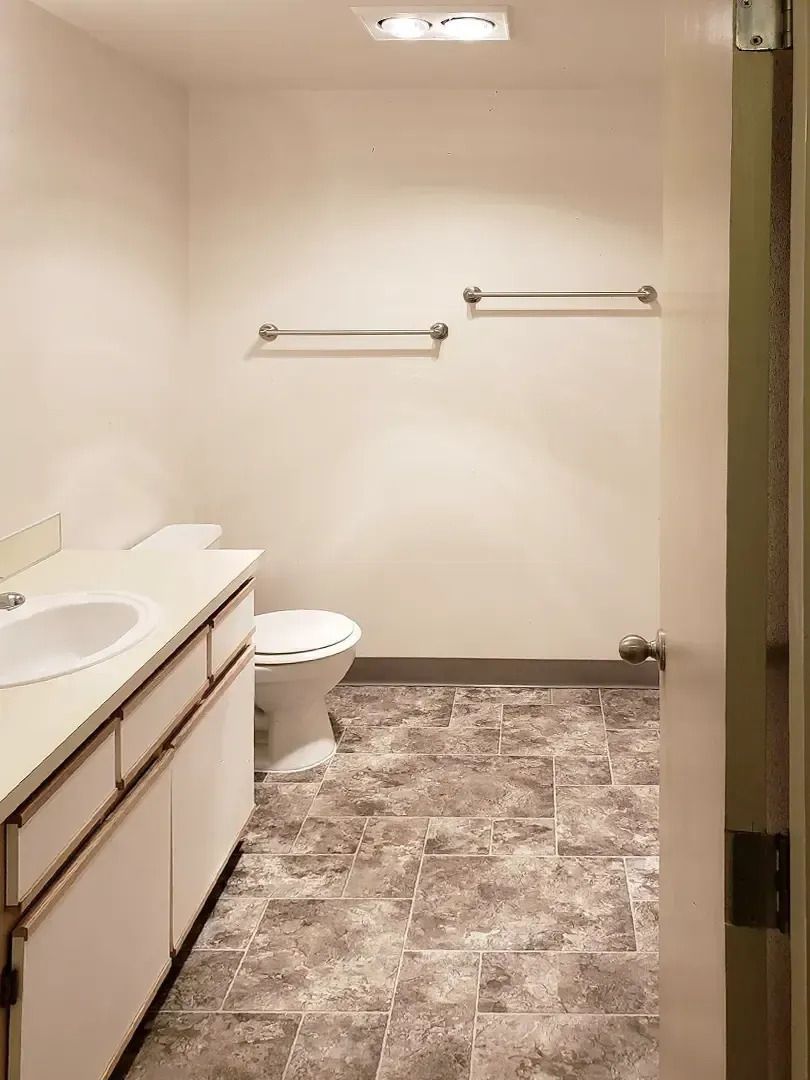 Empty beige bathroom with sink, toilet, towel bars, and patterned tile floor