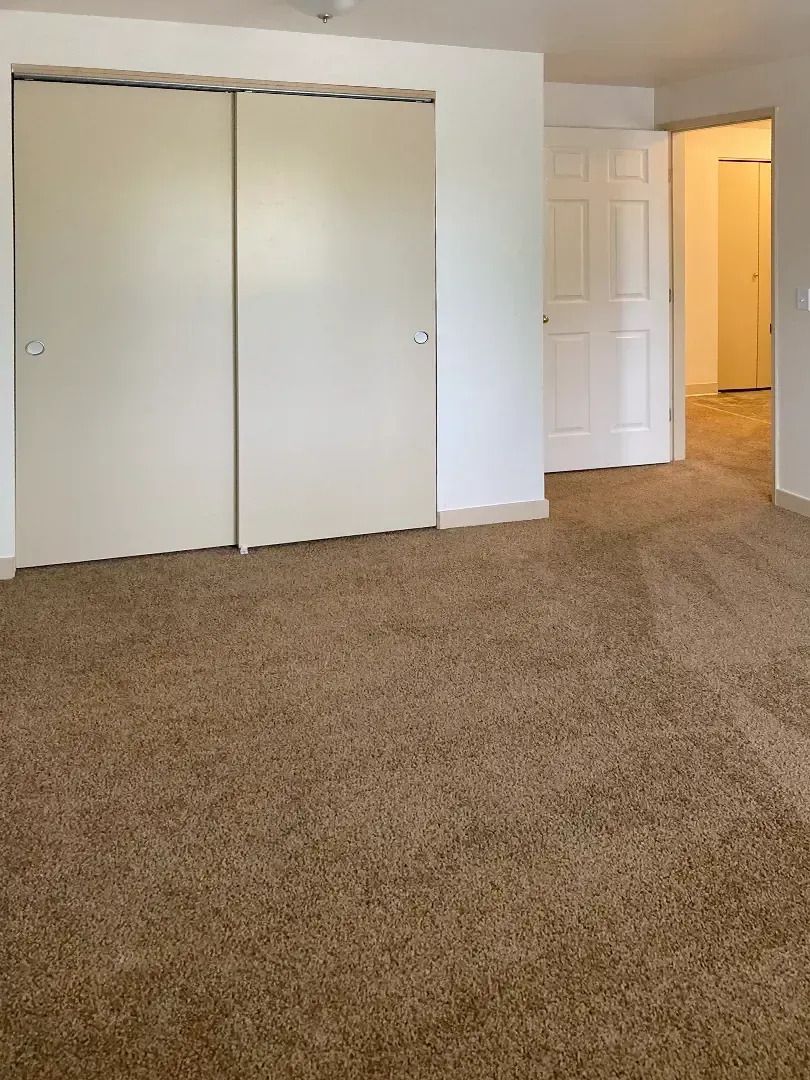 Empty carpeted bedroom with closed closet doors and an open doorway to a lit hall.