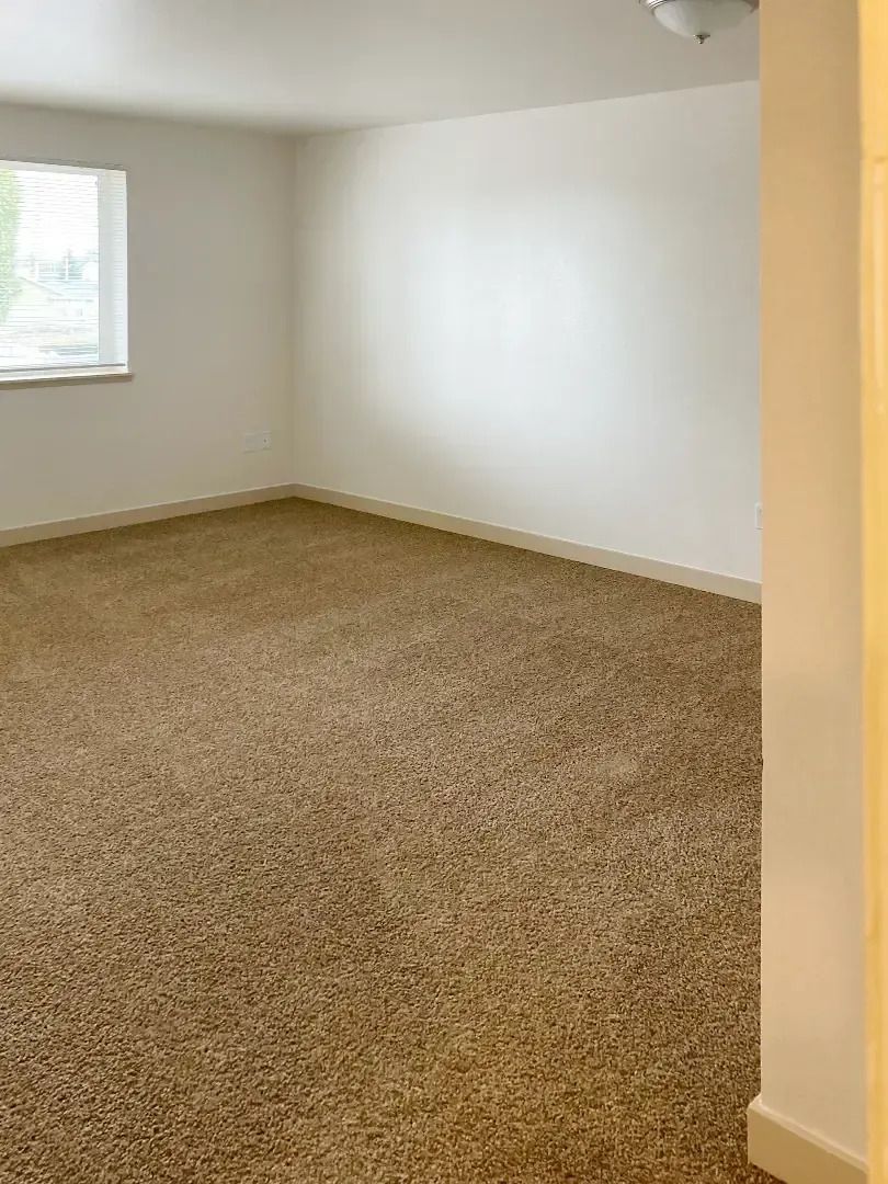 Empty beige carpeted room with white walls and a small window