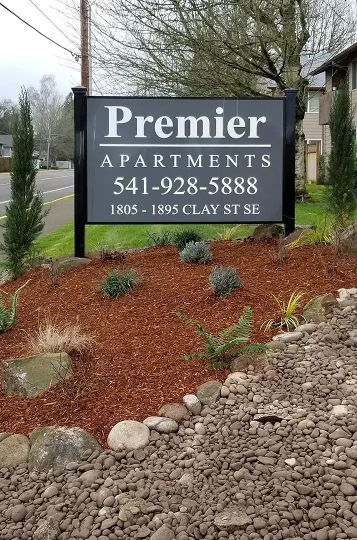 Premier Apartments sign with phone number, set in a landscaped outdoor entrance area