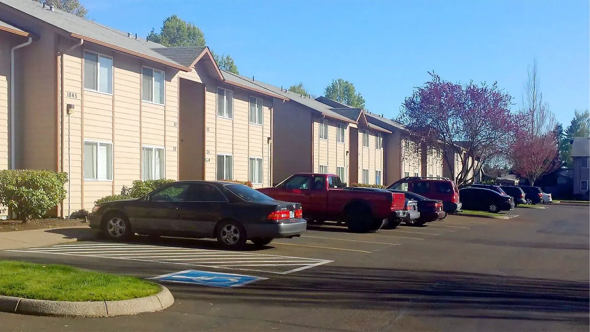Apartment parking lot with several parked cars beside a beige building on a sunny day