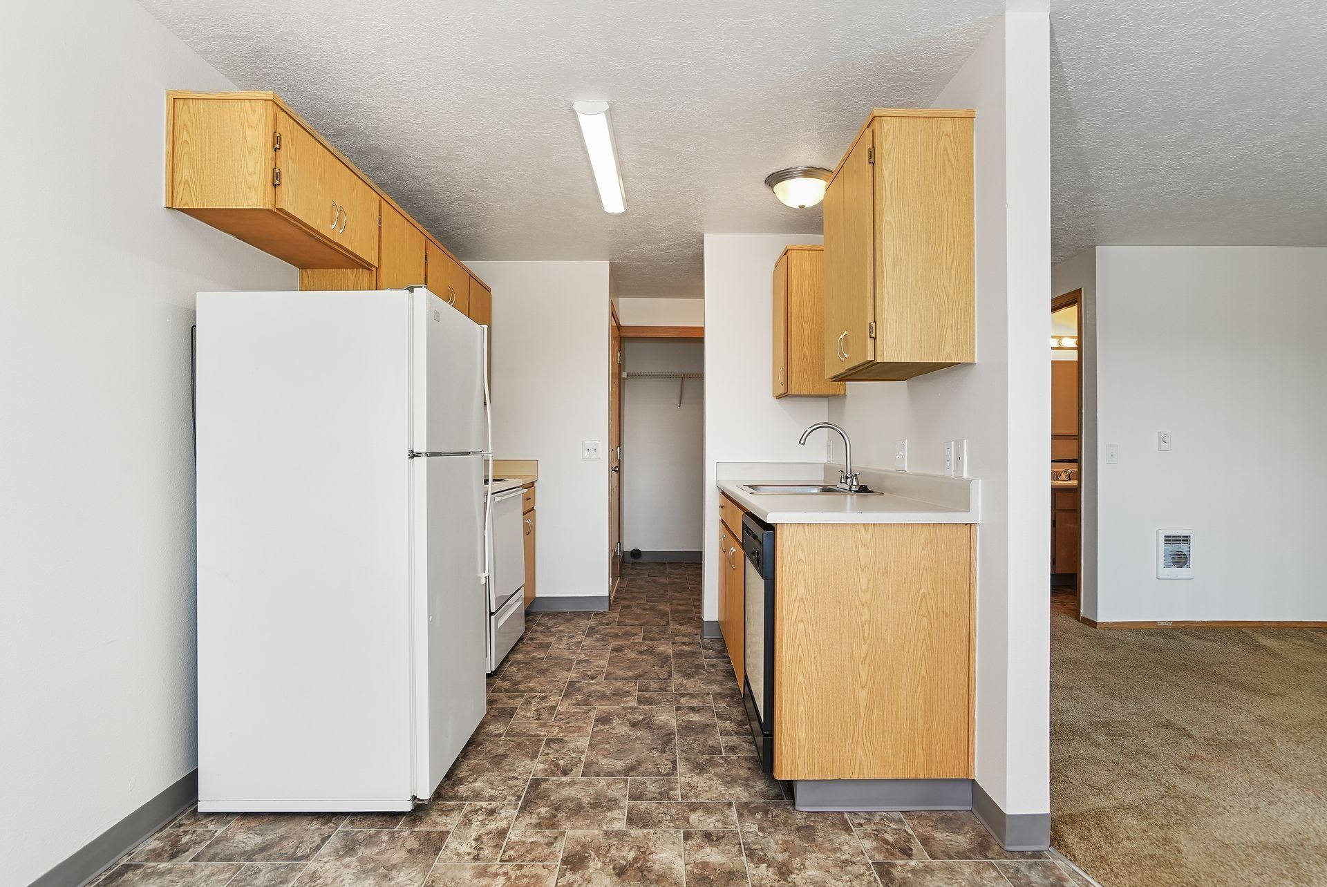Small kitchen with white appliances, light wood cabinets, and patterned floor in a compact apartment.