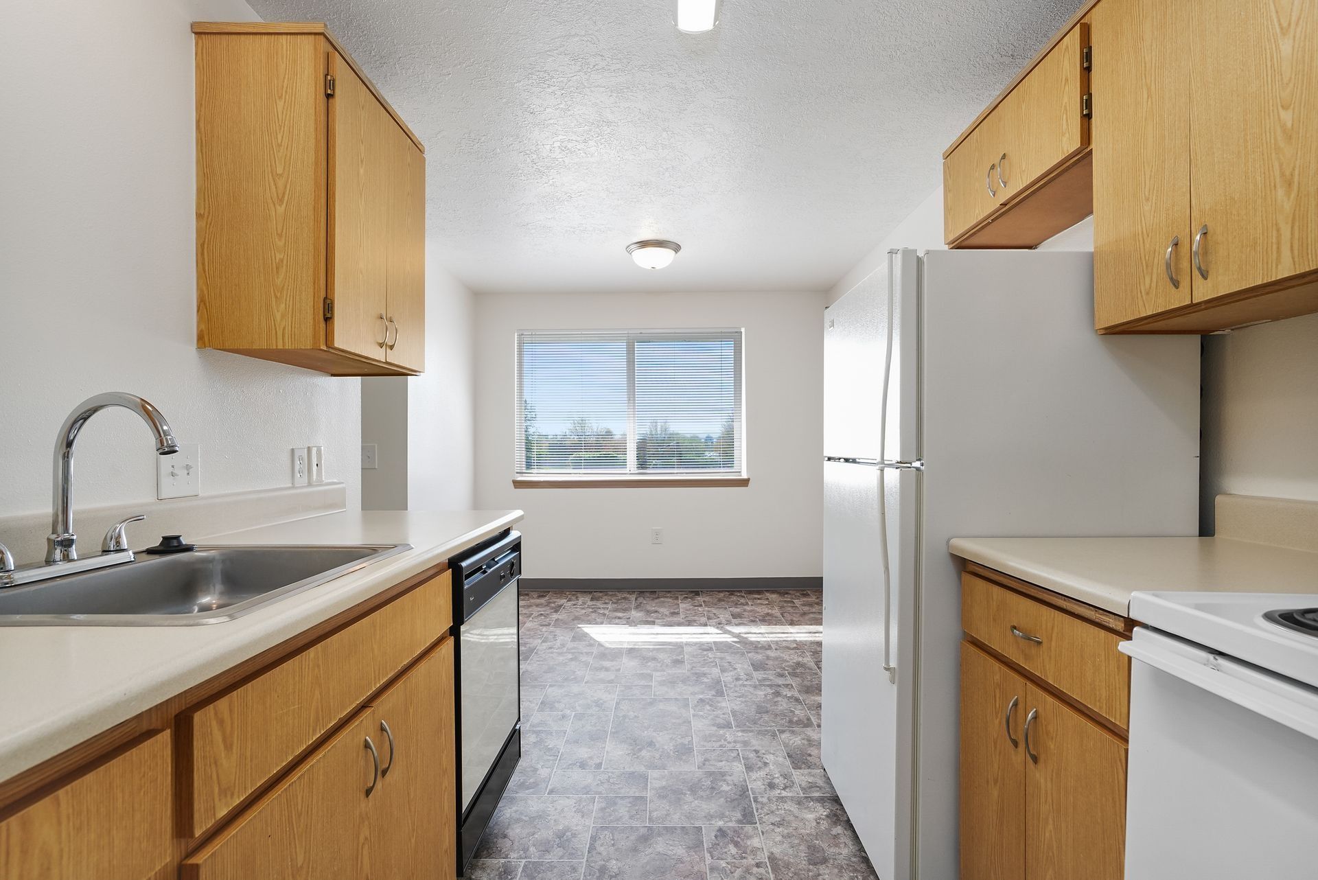 Bright kitchen with wood cabinets, white appliances, and a window at the far end.