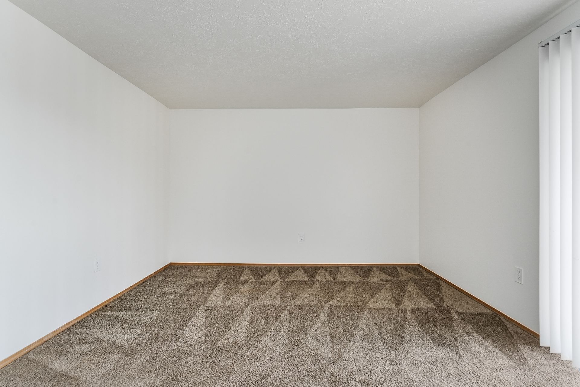 Empty carpeted room with white walls and a window with vertical blinds