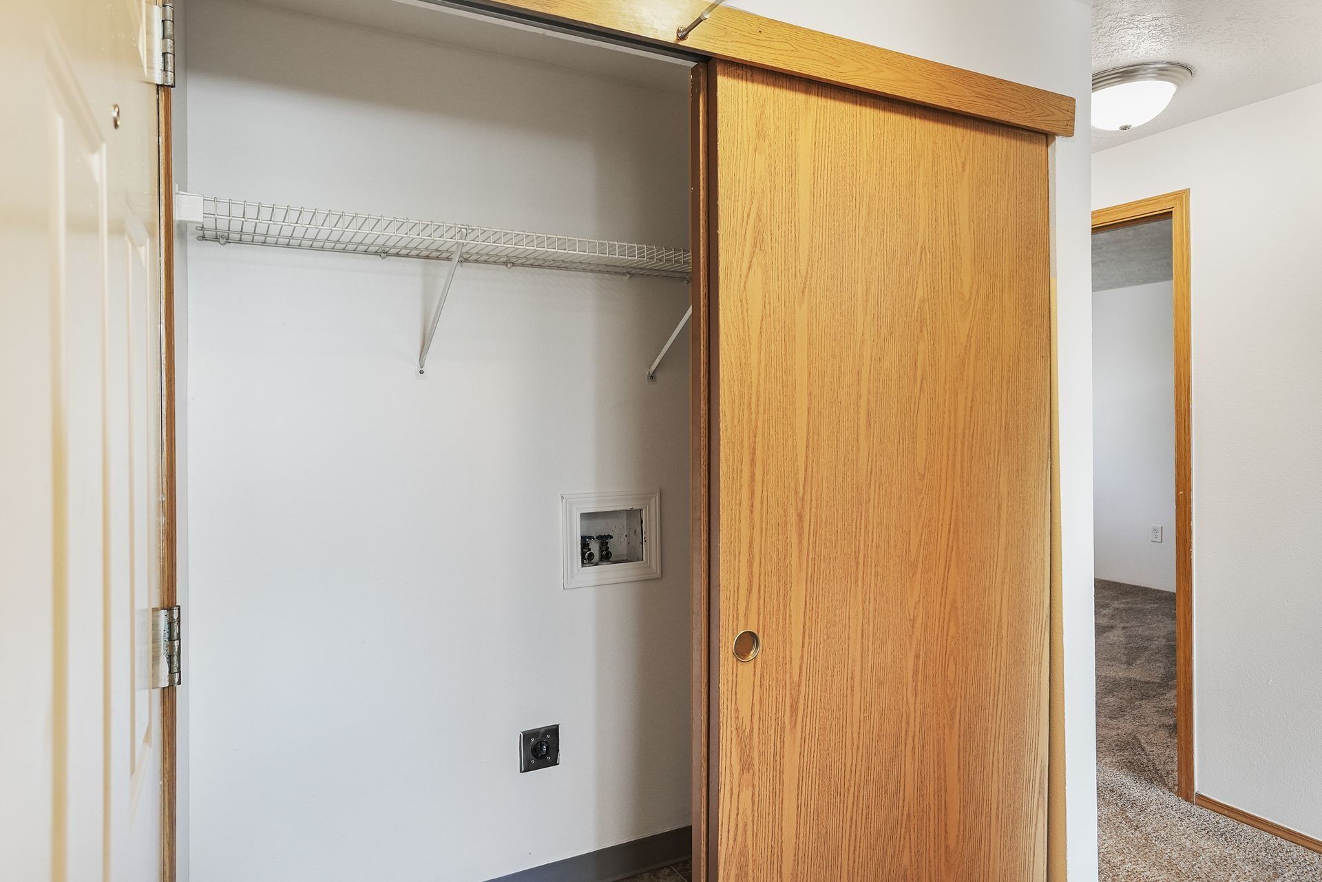 Open closet with a sliding wooden door and white interior in a hallway.