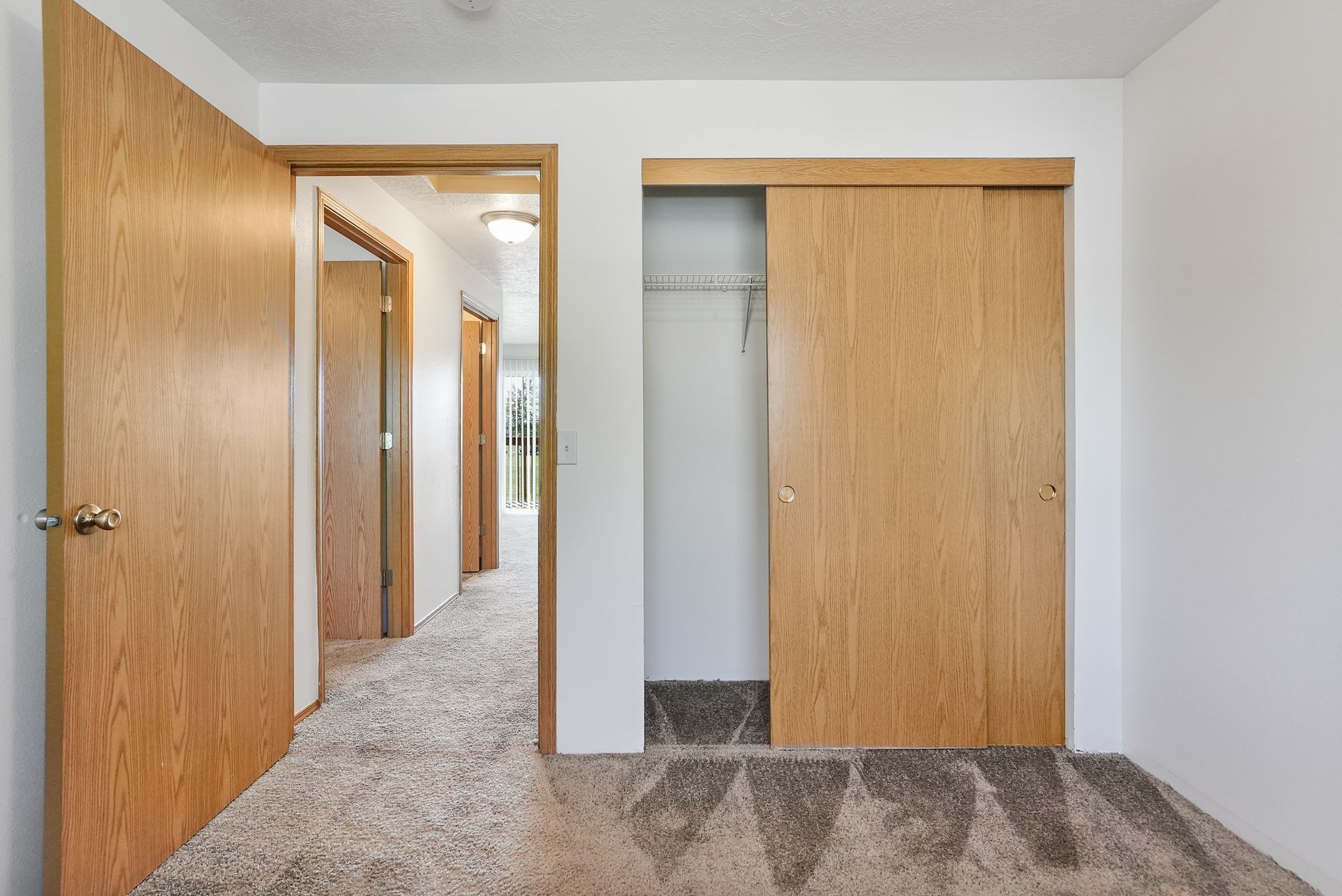 Empty bedroom with open wood doors, carpet, closet, and hallway view