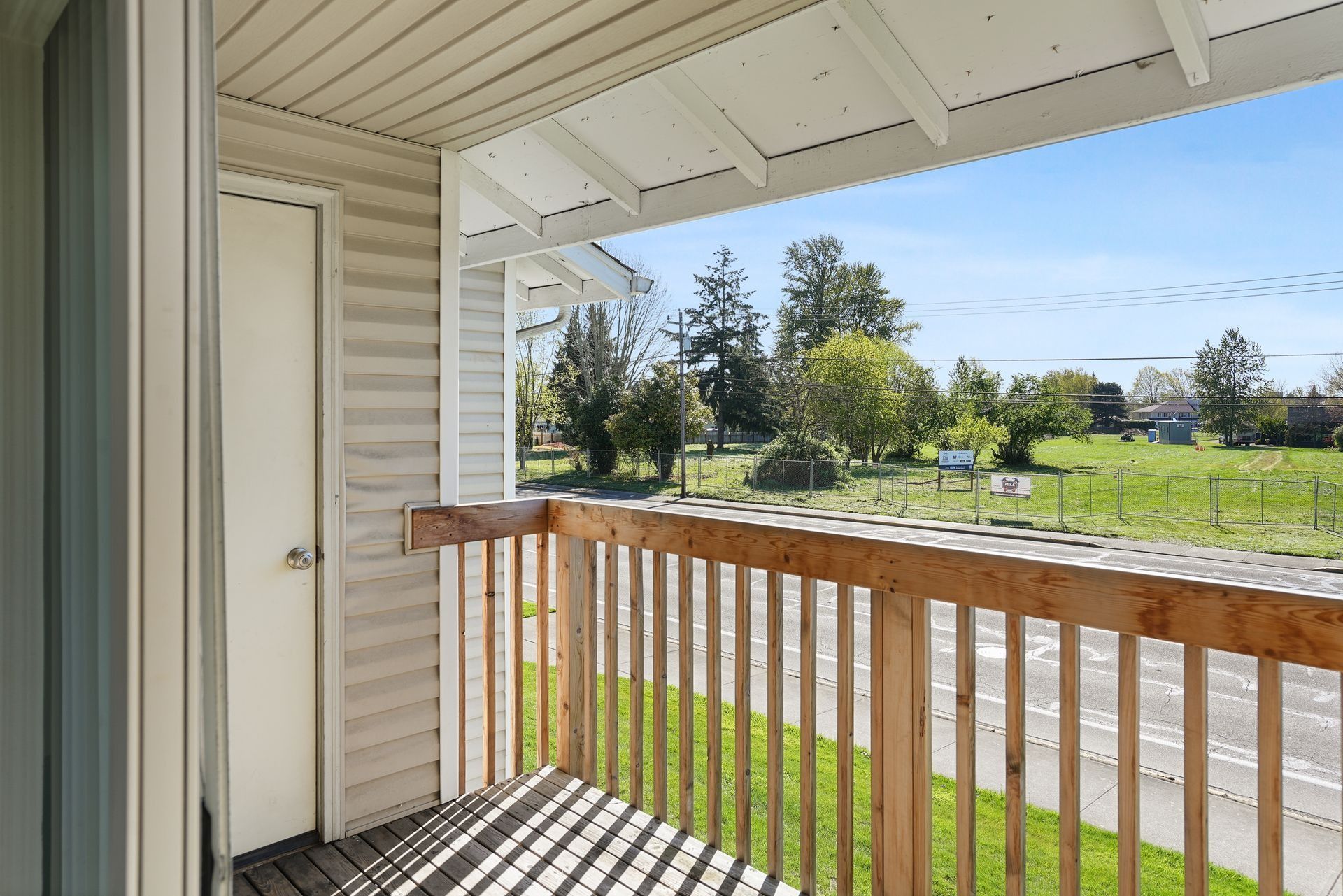 Balcony with wooden railing overlooking a sunny green yard and trees