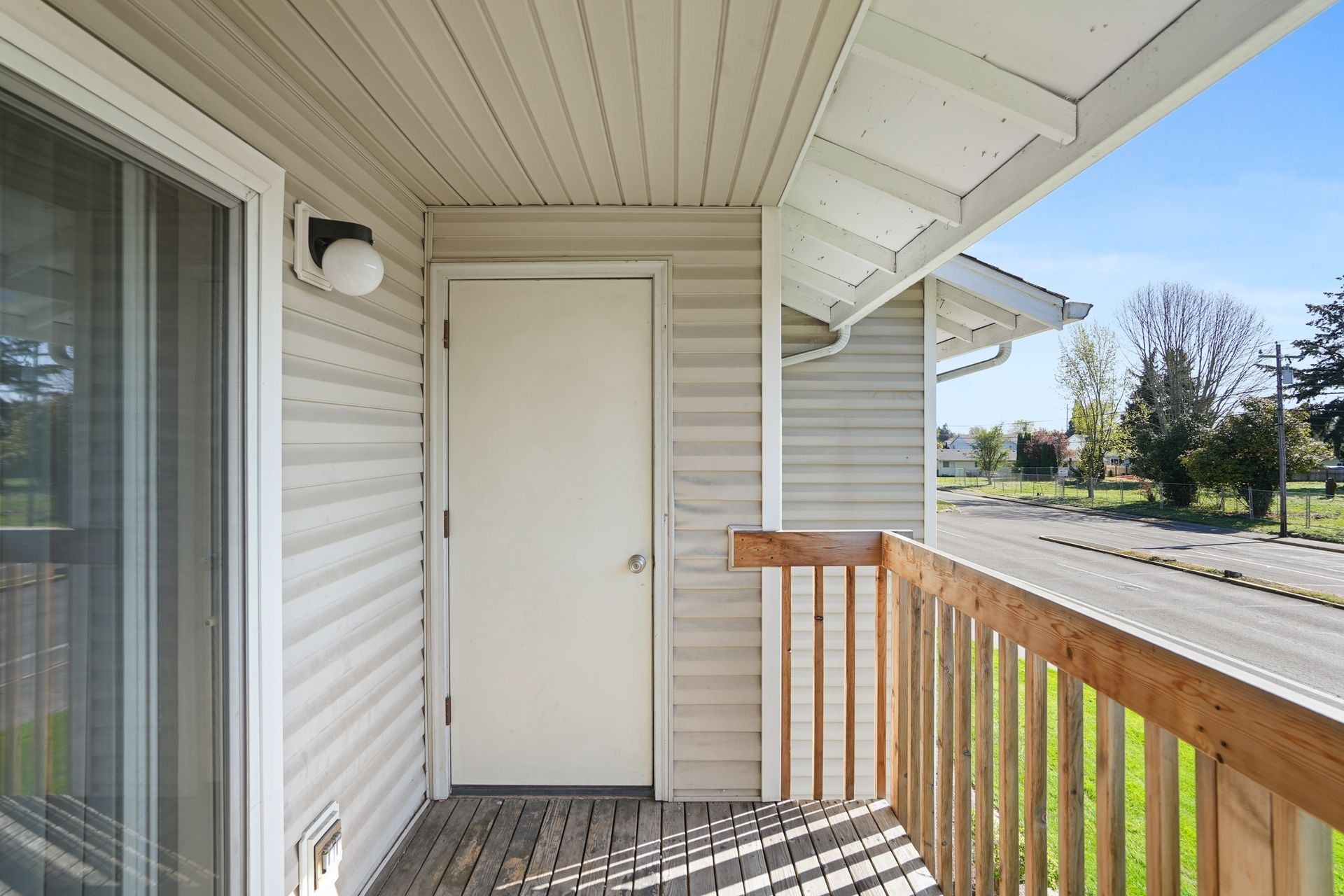 Apartment balcony with white door, beige siding, and wooden railing in bright daylight