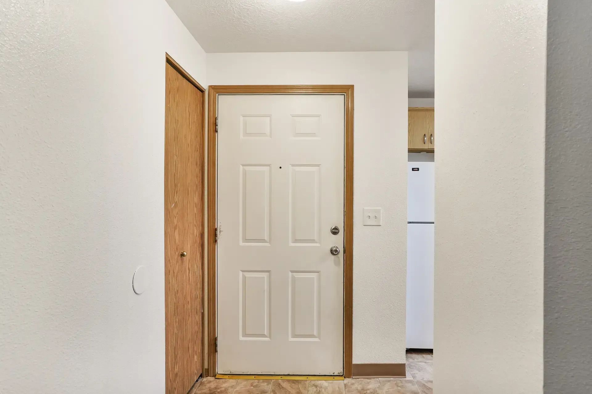 Front entryway with a white door, wood trim, and a glimpse of a kitchen beyond.